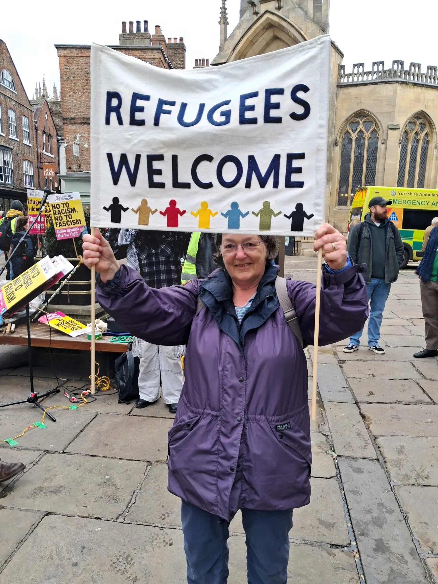 Mary holding a banner with words Refugees Welcome.