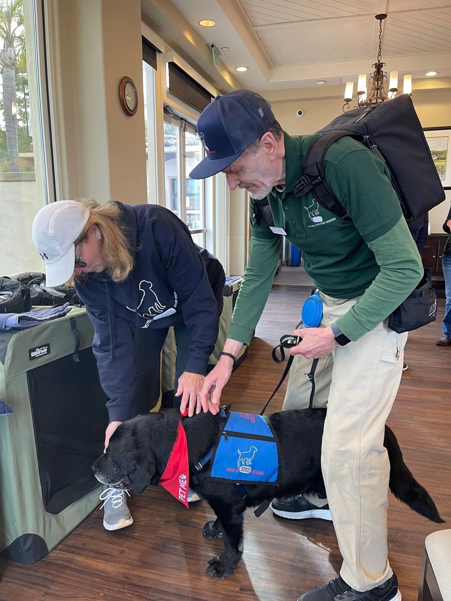 Freedom Dogs volunteers greeting a black Labrador service dog wearing a Freedom Dogs vest