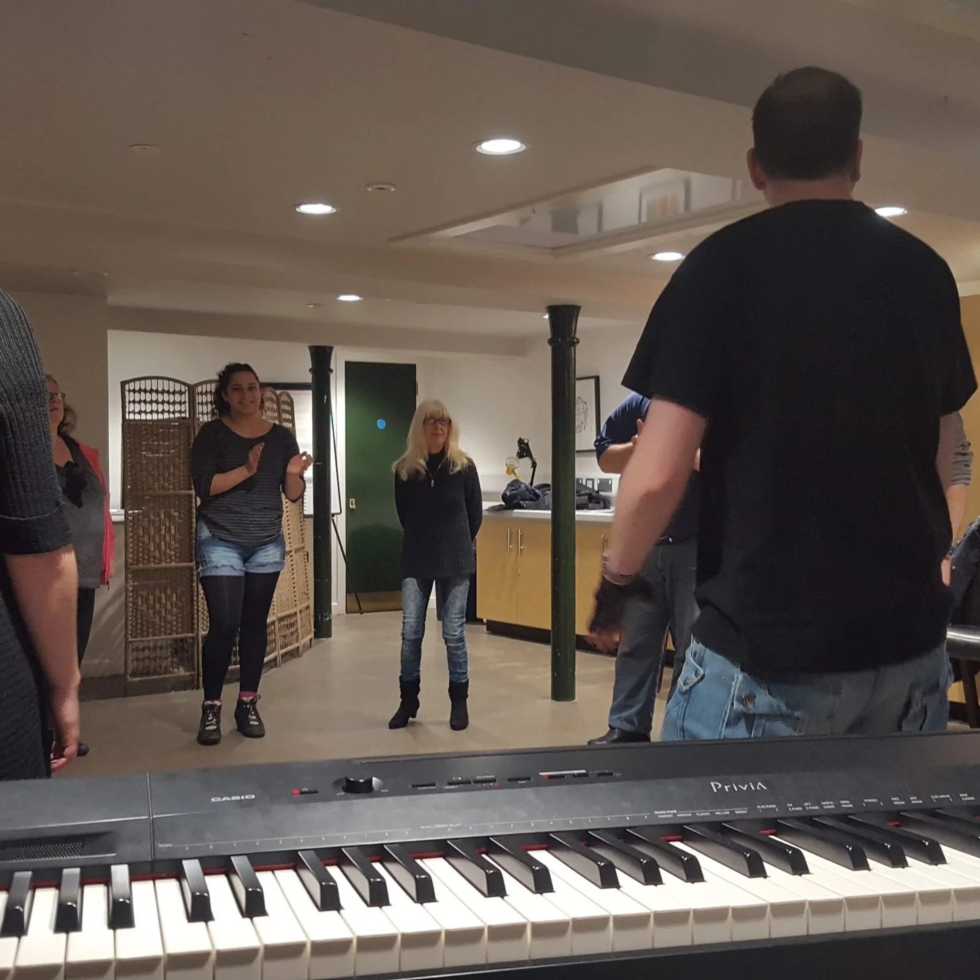 A group of people standing the other side of a keyboard, all engaged in a musical improv workshop in Nottingham