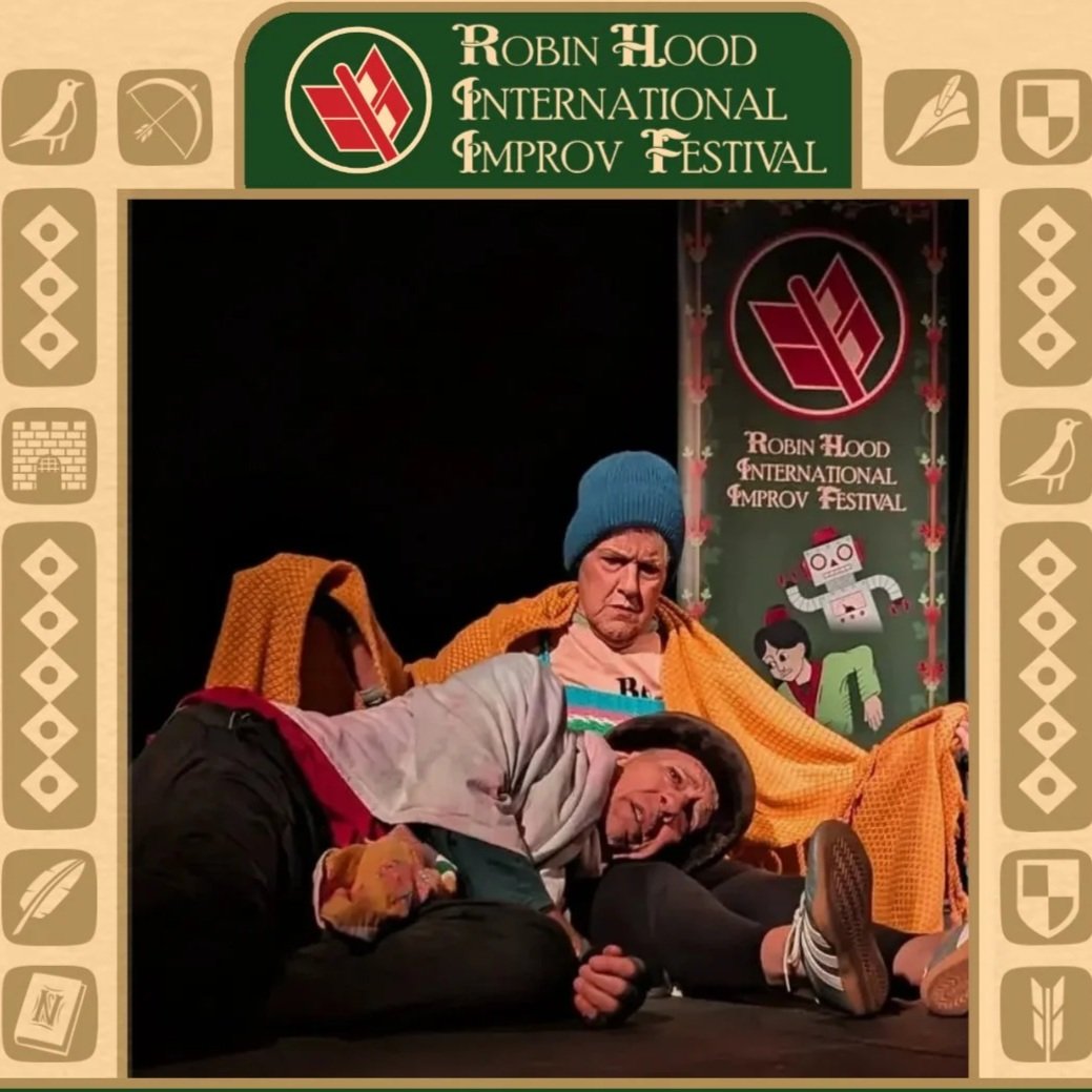 A picture of a male and female improviser on stage covered in blankets with a Robin Hood International Improv Festival banner behind them