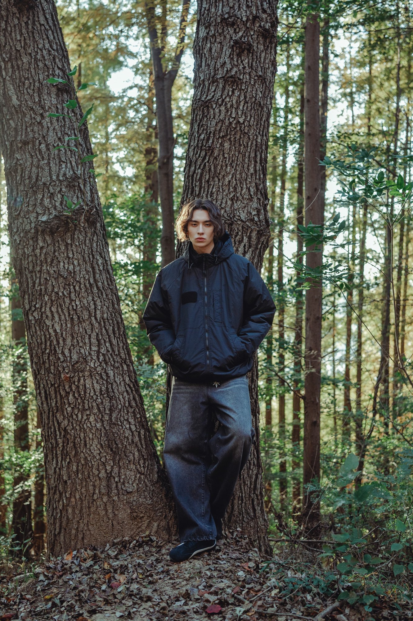 Lookbook photograph of a male model leaning against a tree in a forest