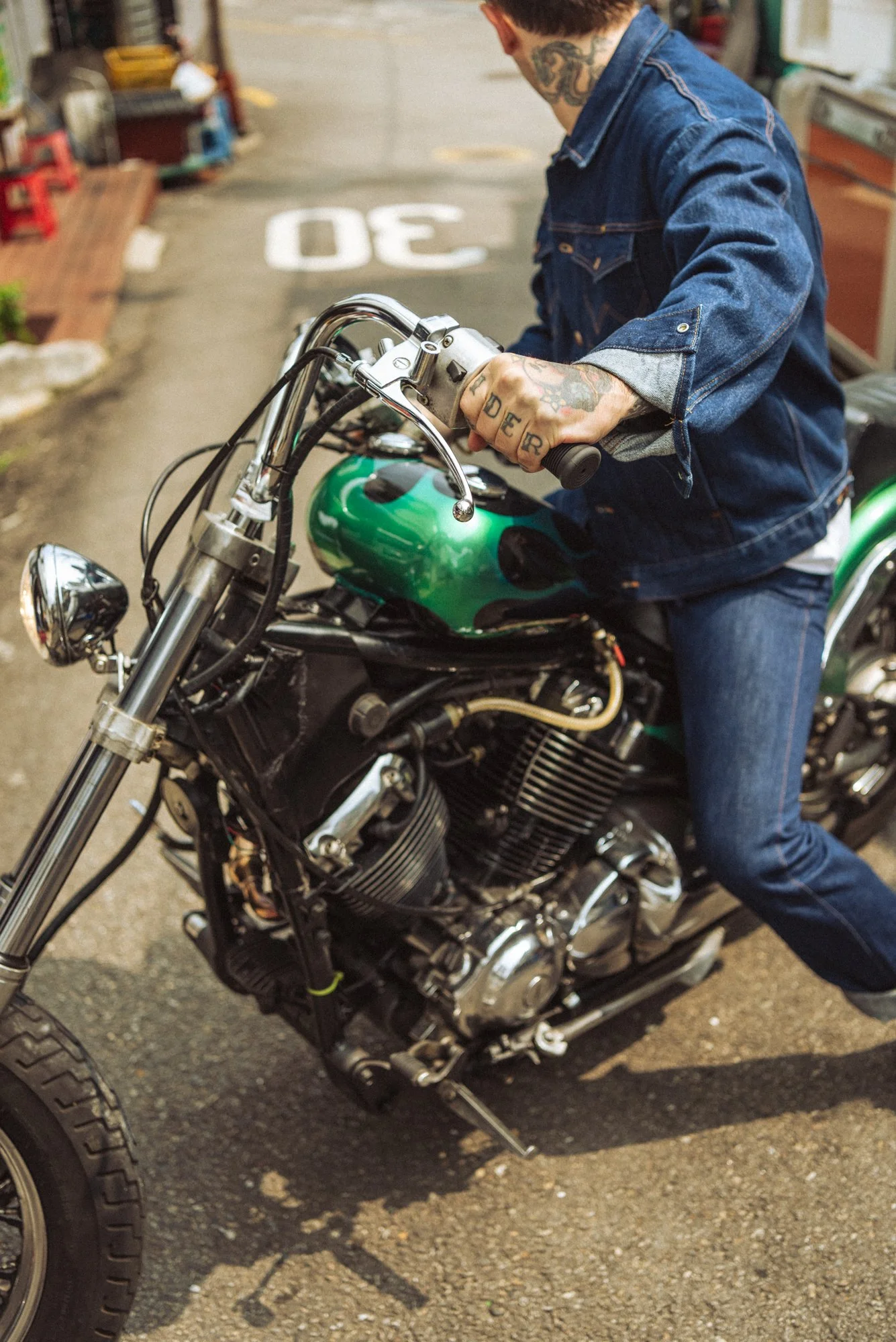 Fashion photograph of a tattooed man riding a motorbike wearing denim