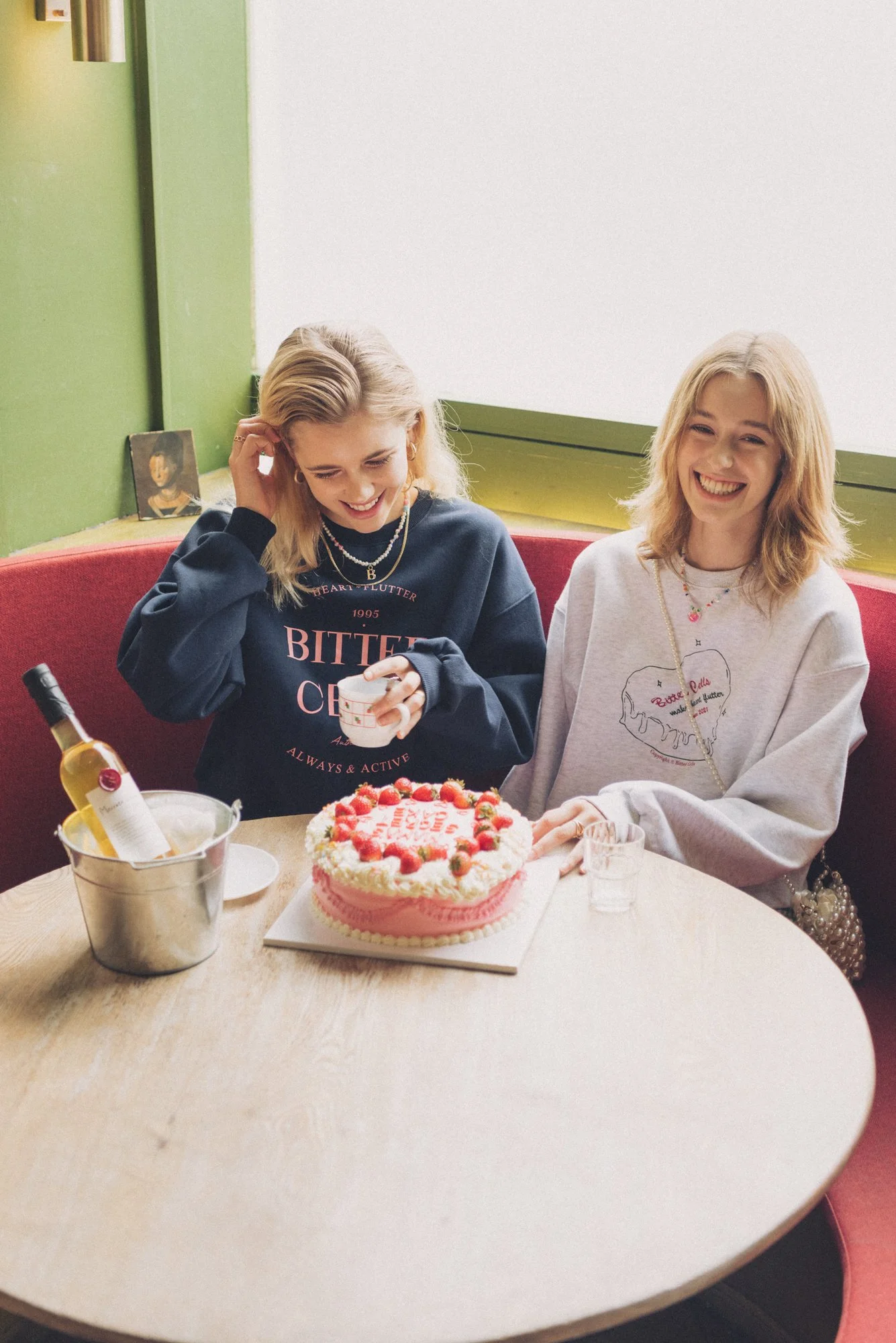 Fashion editorial photograph of two women with cake and wine