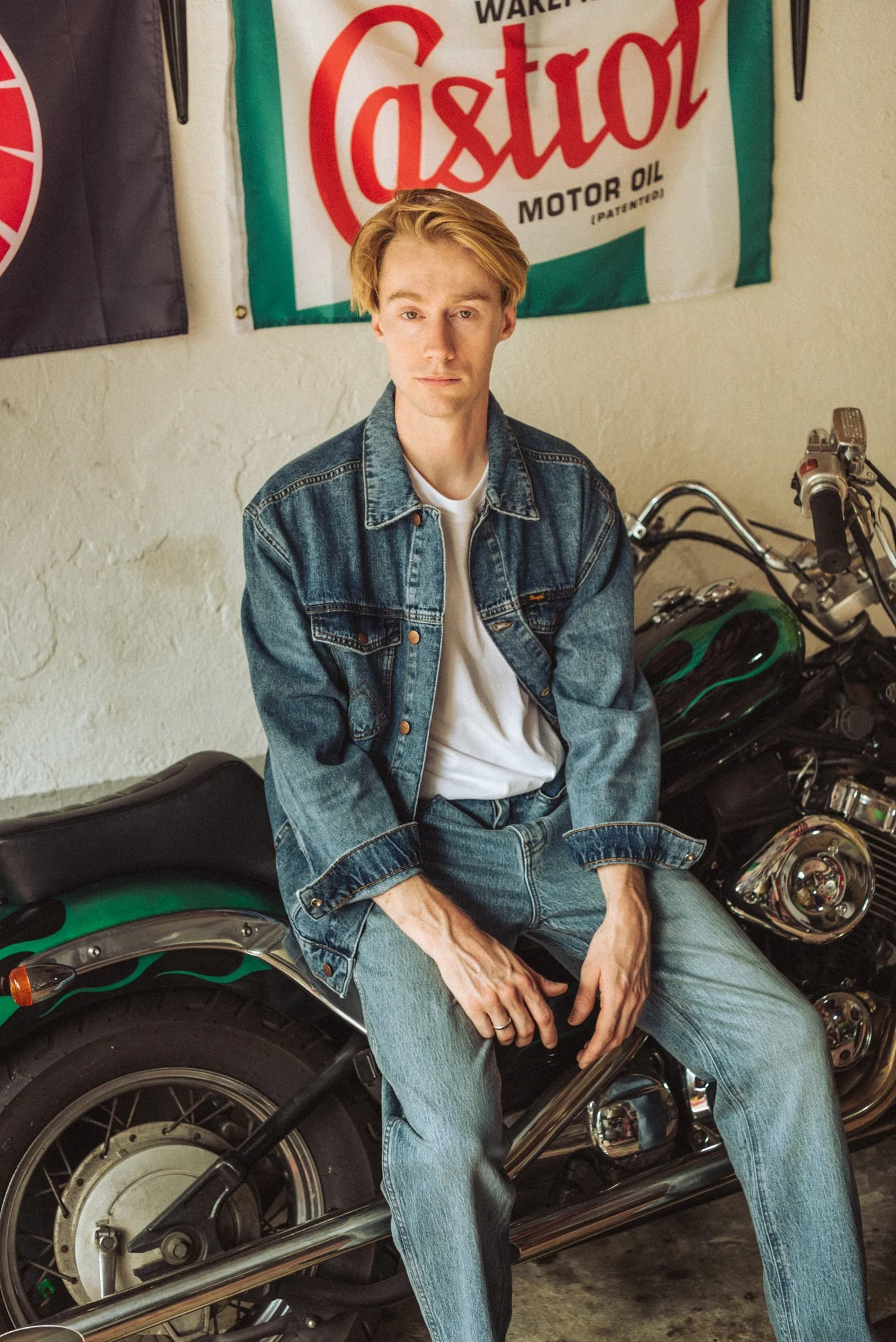 Fashion photograph of a male model sitting on a motorbike wearing denim