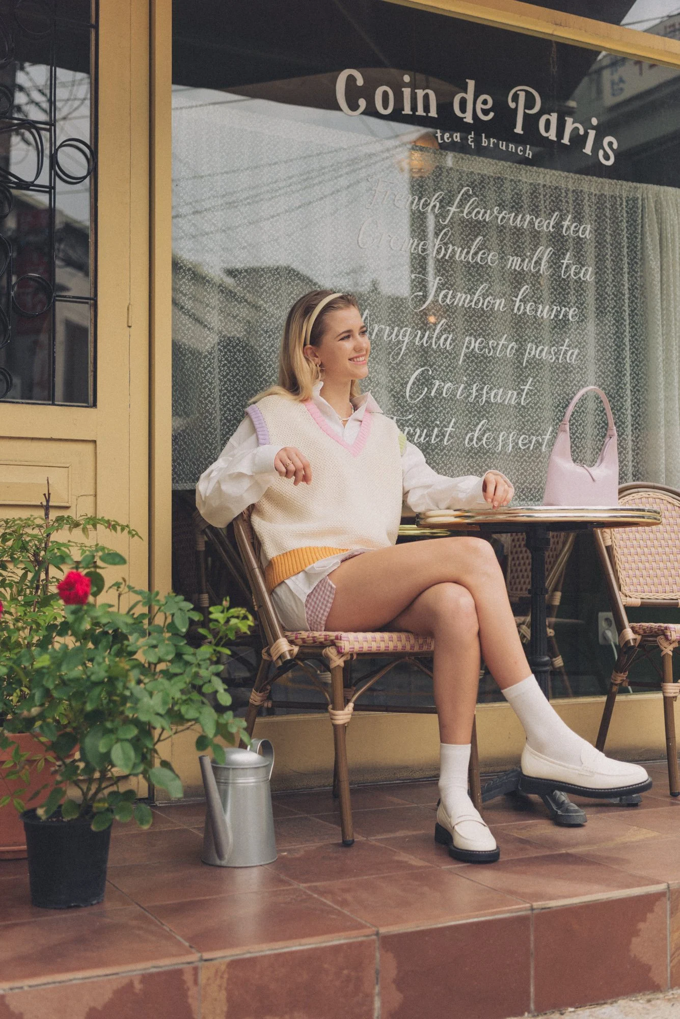 Fashion photograph of a female model at a cafe wearing preppy clothing