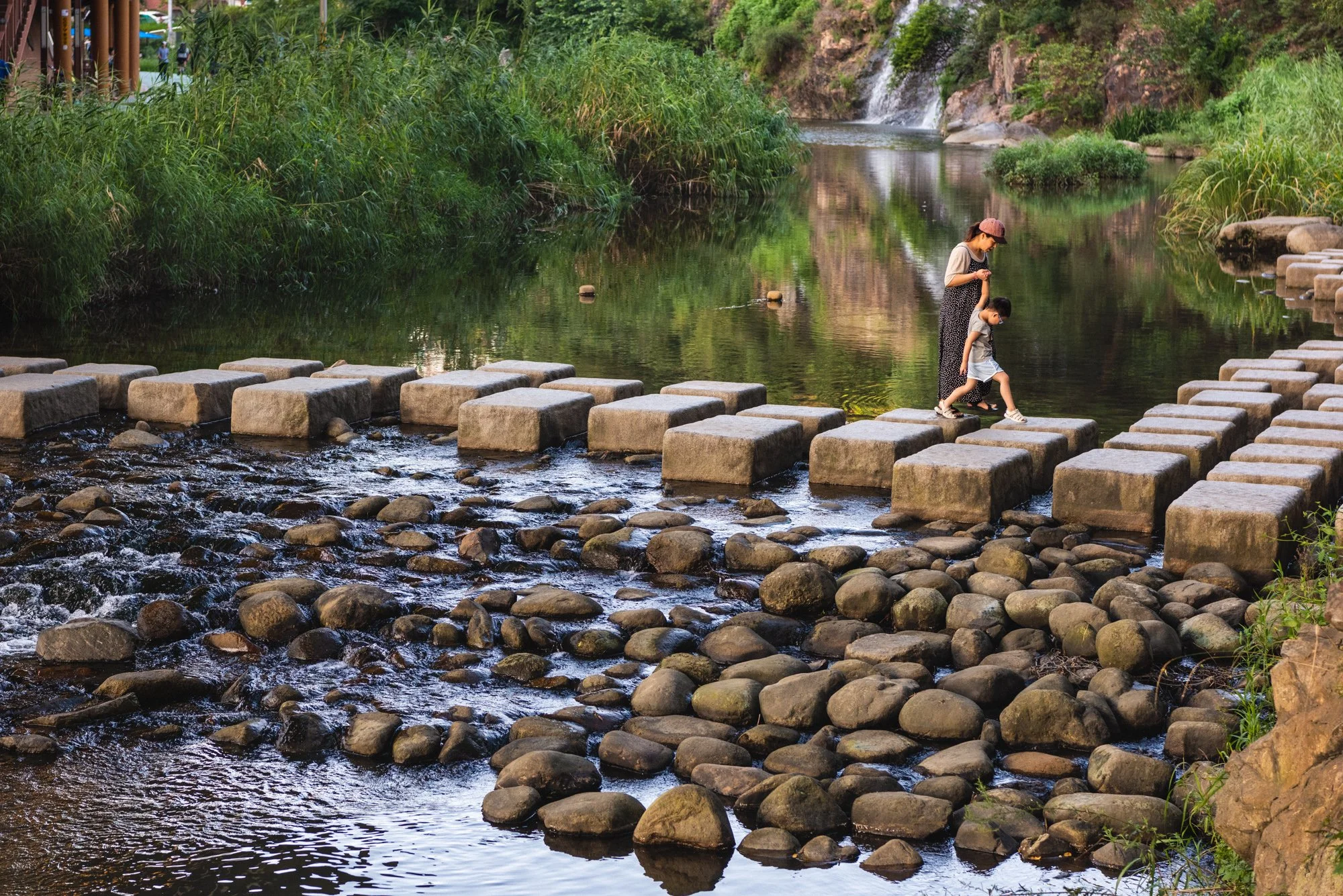 A mother helps her son cross a stone bridge near a waterfall in the Hongjecheon stream in Seoul, South Korea