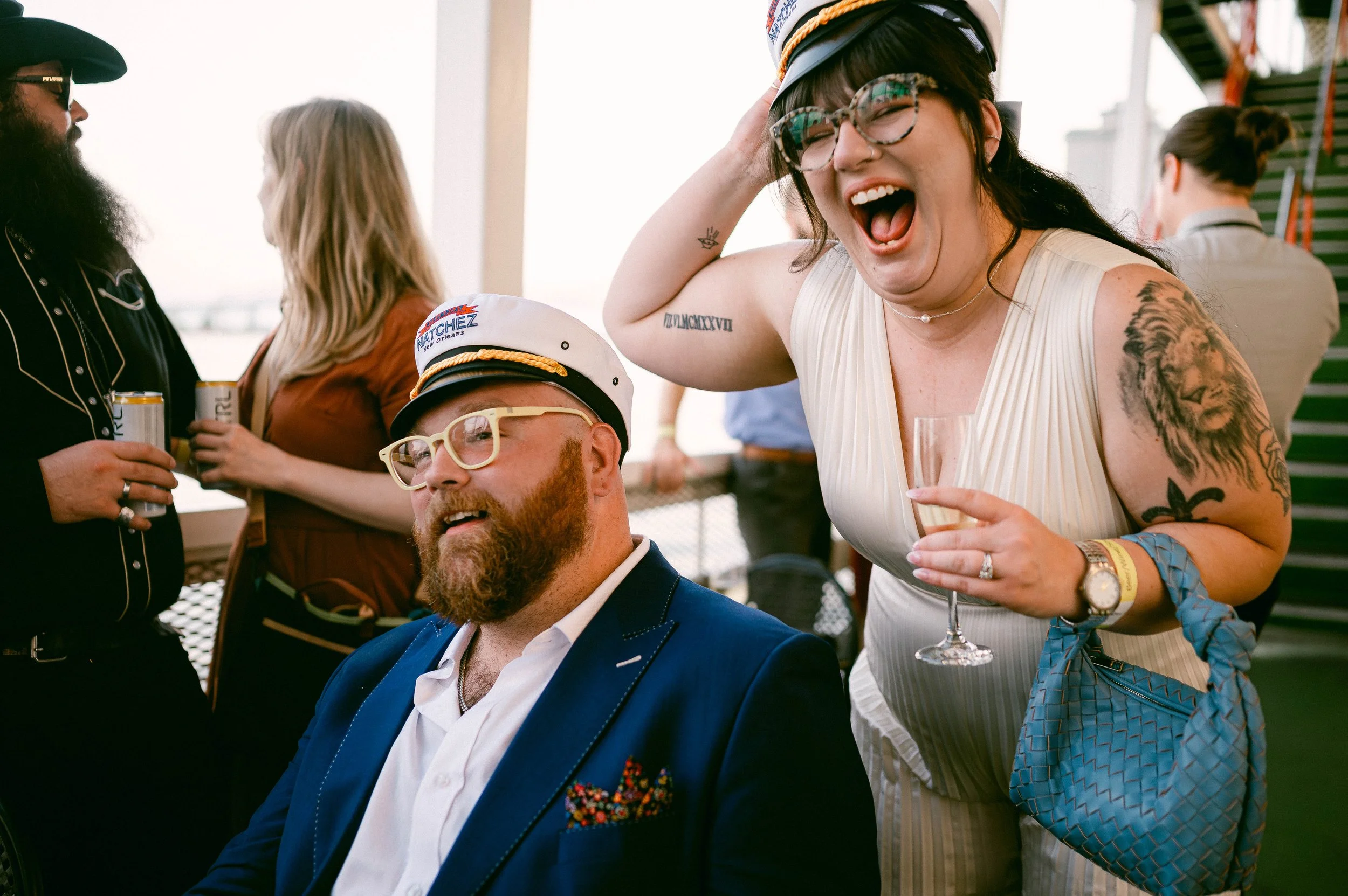 Newlyweds aboard a steamboat in New Orleans cheer and celebrate while wearing captain's hats.
