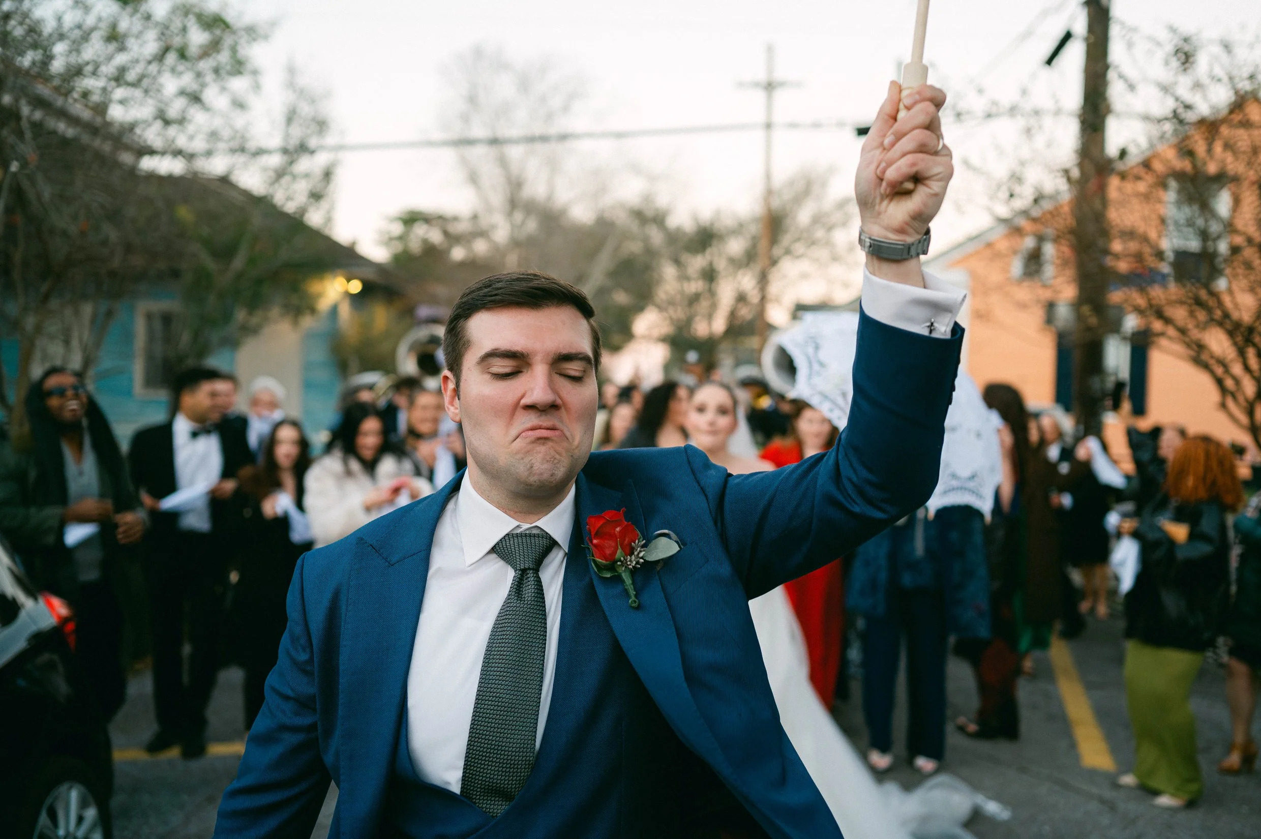 A groom dancing at his wedding second line in New Orleans, with a crowd of guests in the background.