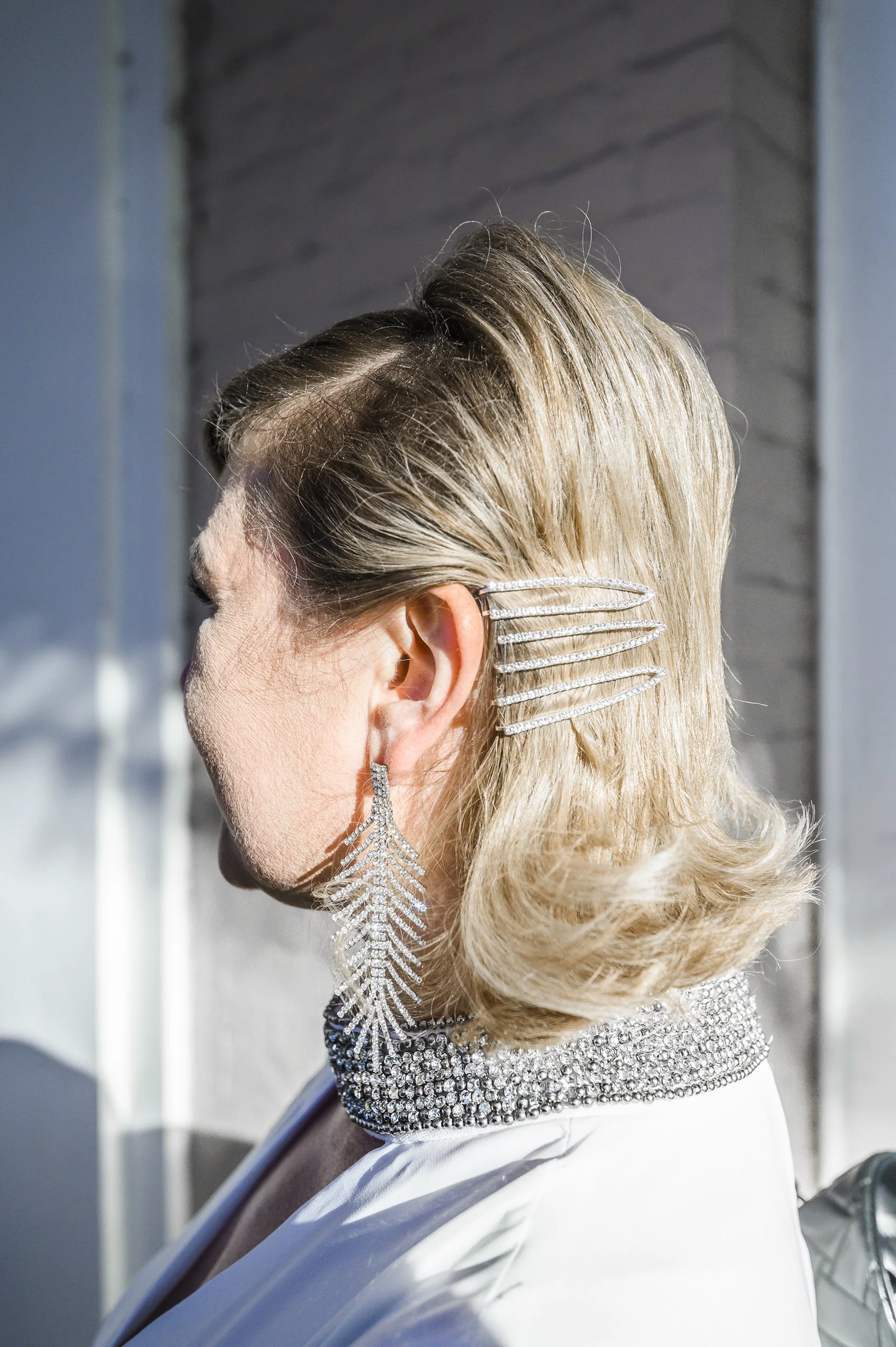 Side profile of bride with blonde hair styled in vintage waves, wearing a sparkling rhinestone dress, large rhinestone earrings, and decorative hair clips.
