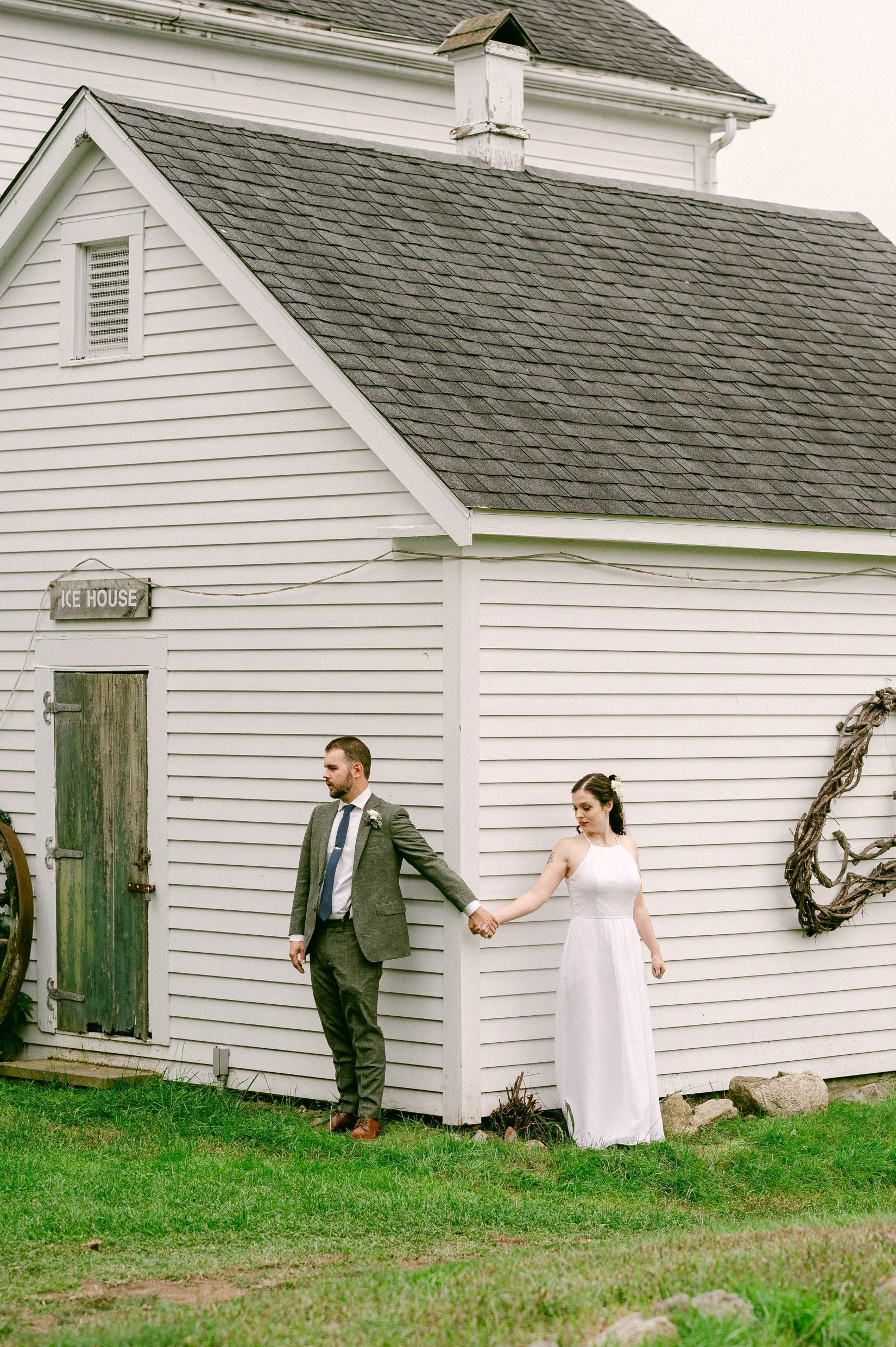 A bride and groom holding hands outside a white wooden building before seeing each other for the first look on their wedding day.
