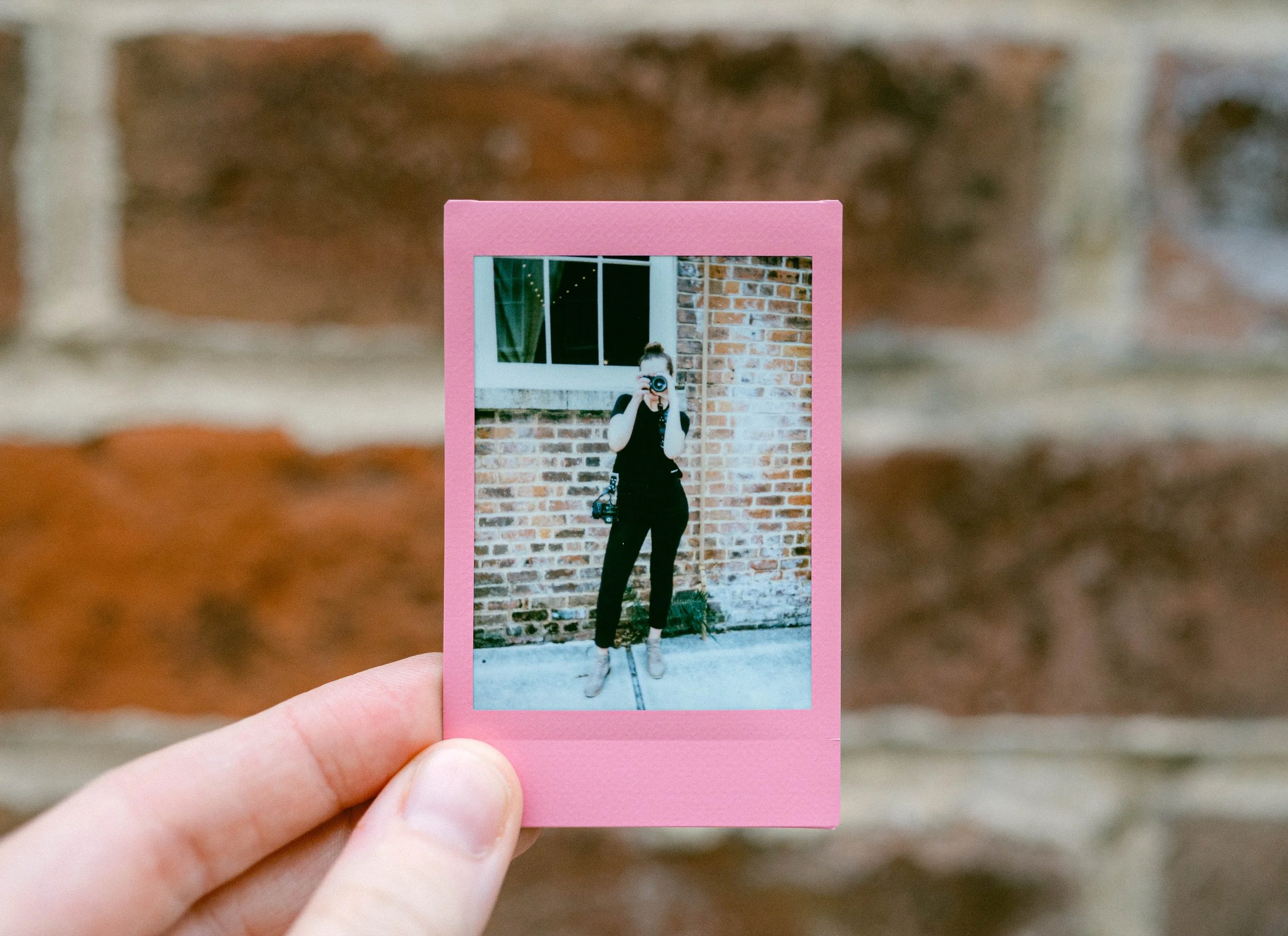 Hand holding an instant photo showing a photographer taking a picture.