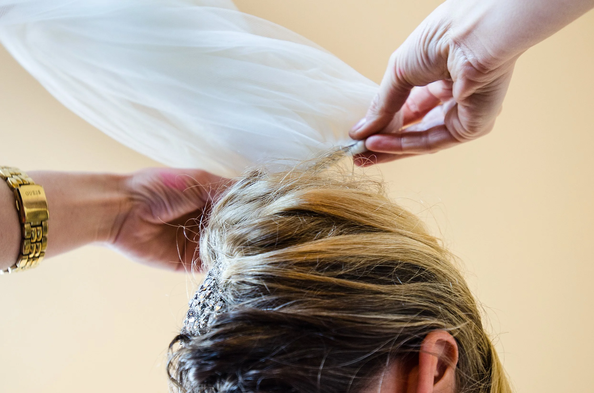 Two hands place a veil on top of a bride's finished hair while preparing for her wedding.