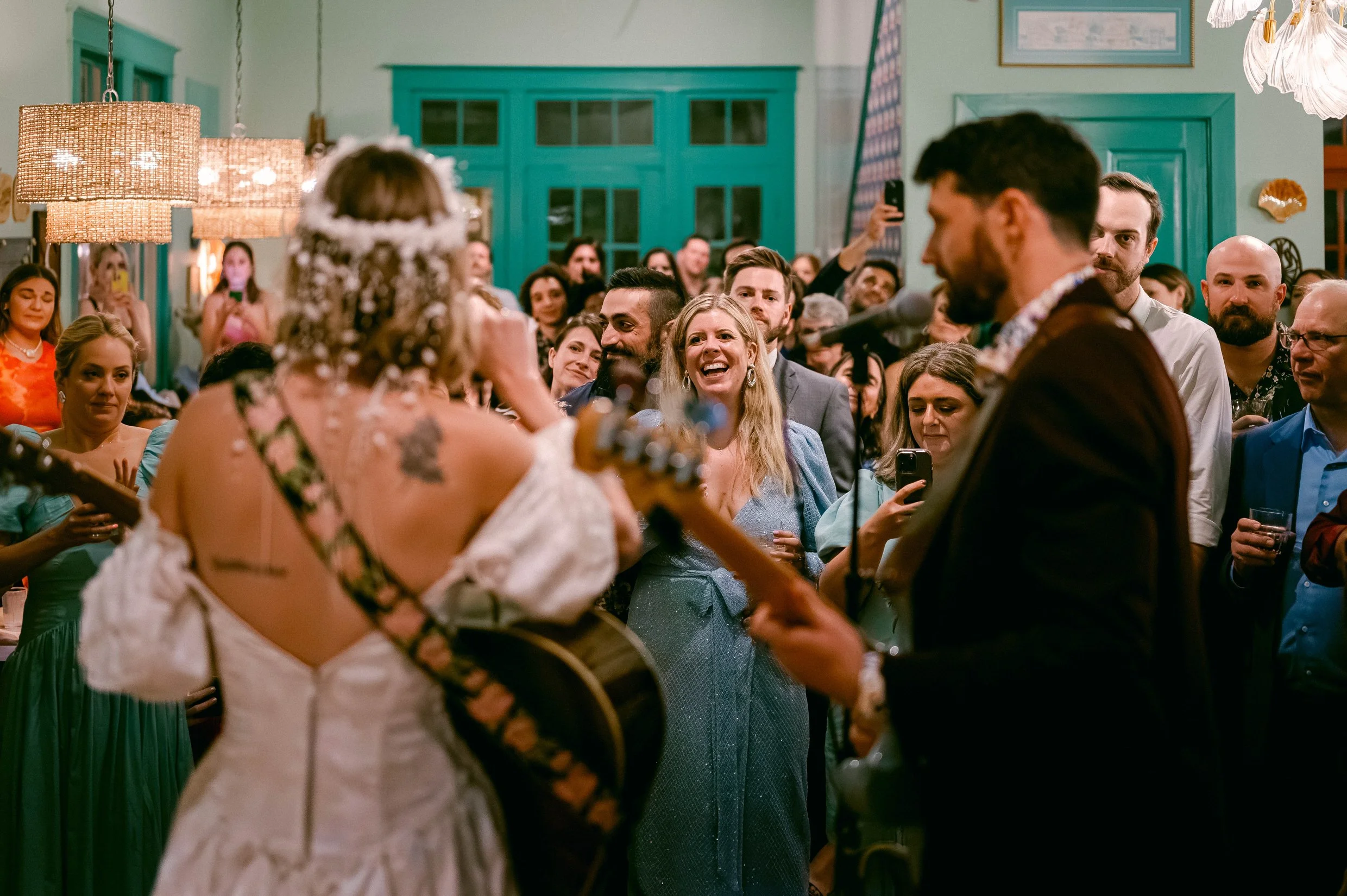 A wedding ceremony with a bride and groom playing guitars and a lively crowd watching and taking photos.