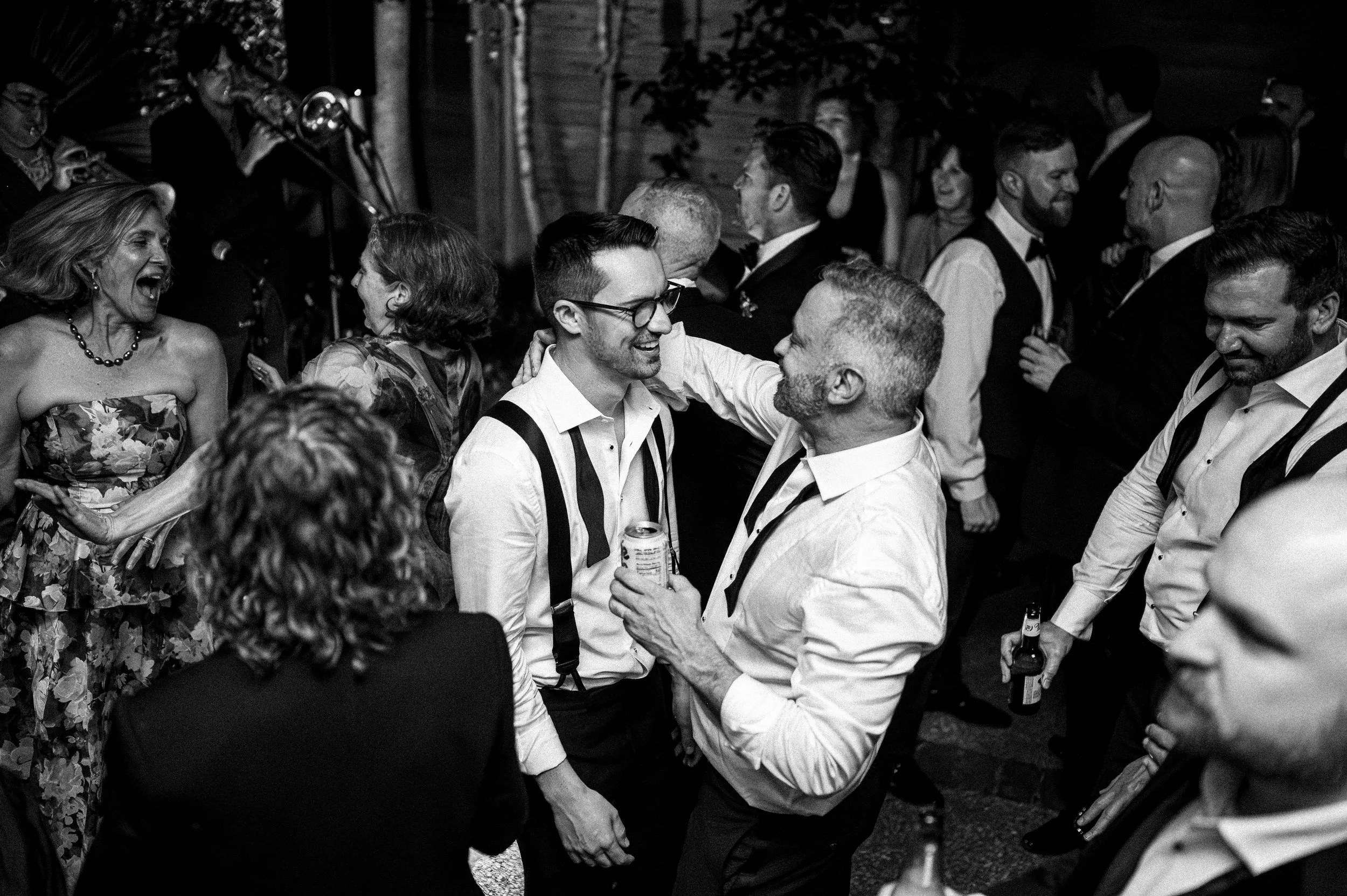 Gay couple dances at their New Orleans wedding surrounded by other people, with a live band performing in the background.