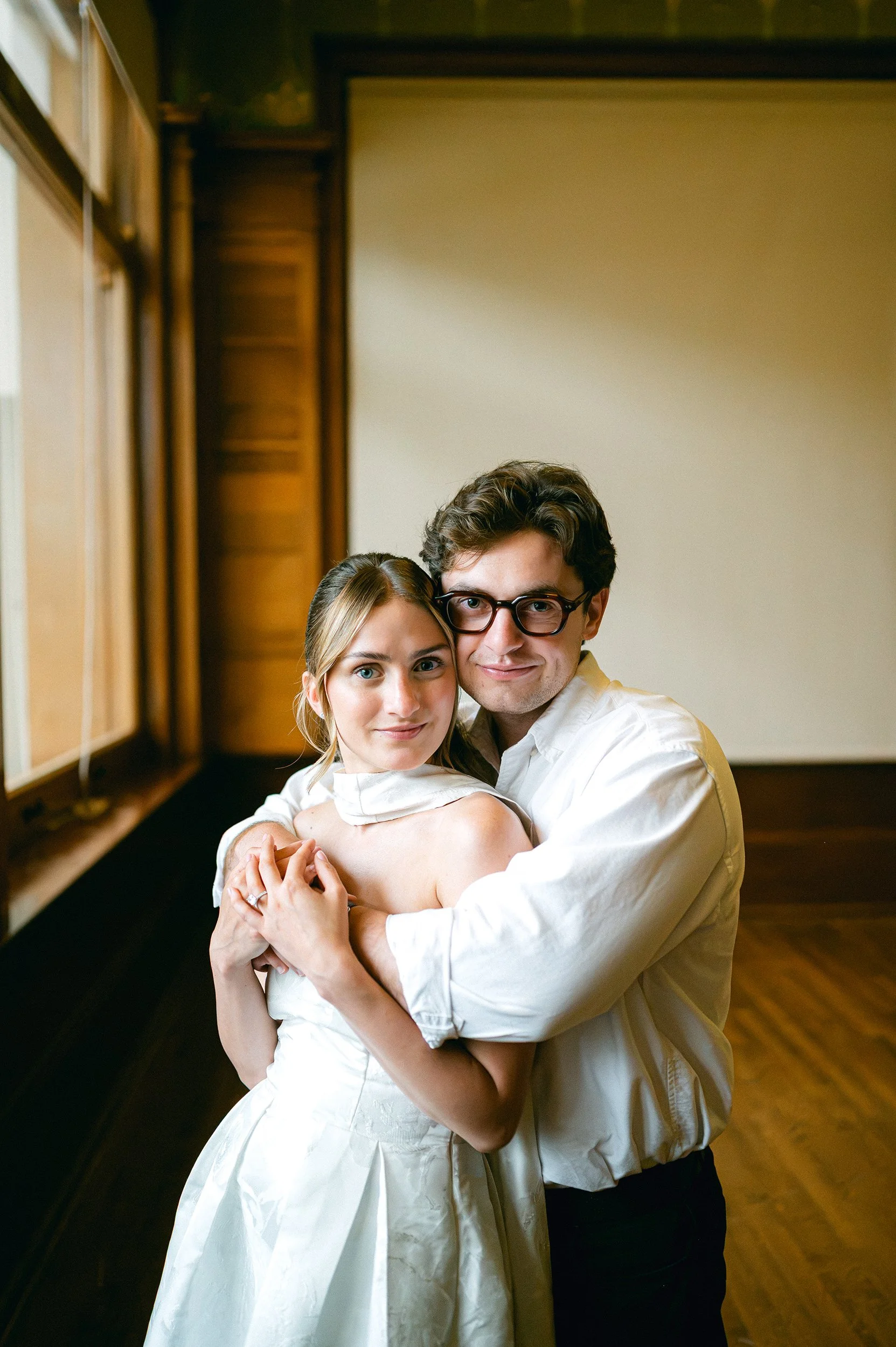 A young engaged couple is embracing each other inside a room with wooden paneling and a projector screen.