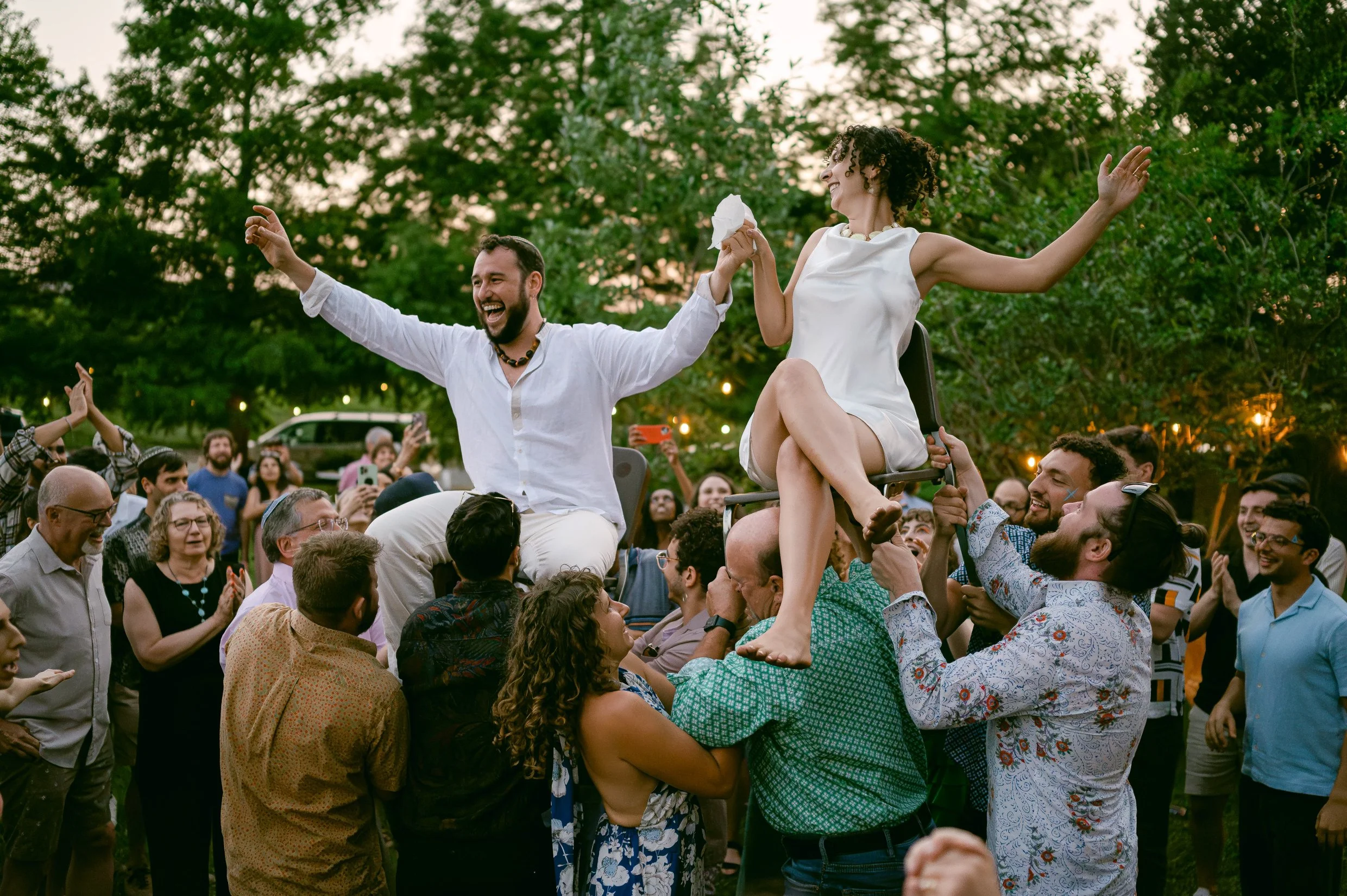 A bride and groom being lifted into the air during the hora at their outdoor wedding.