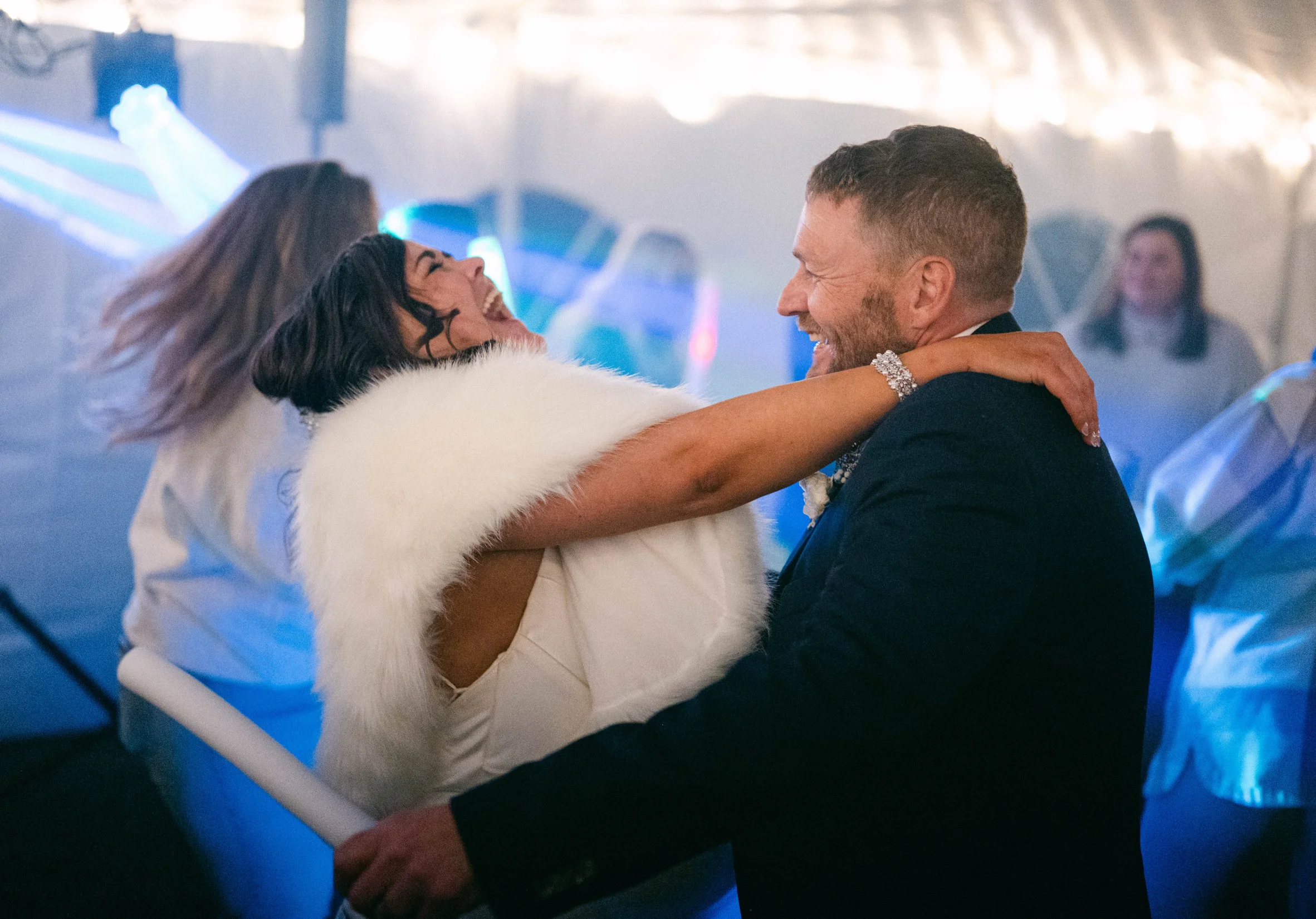 A joyful newlywed couple dancing together at their wedding, both smiling and embracing each other in a festive atmosphere.