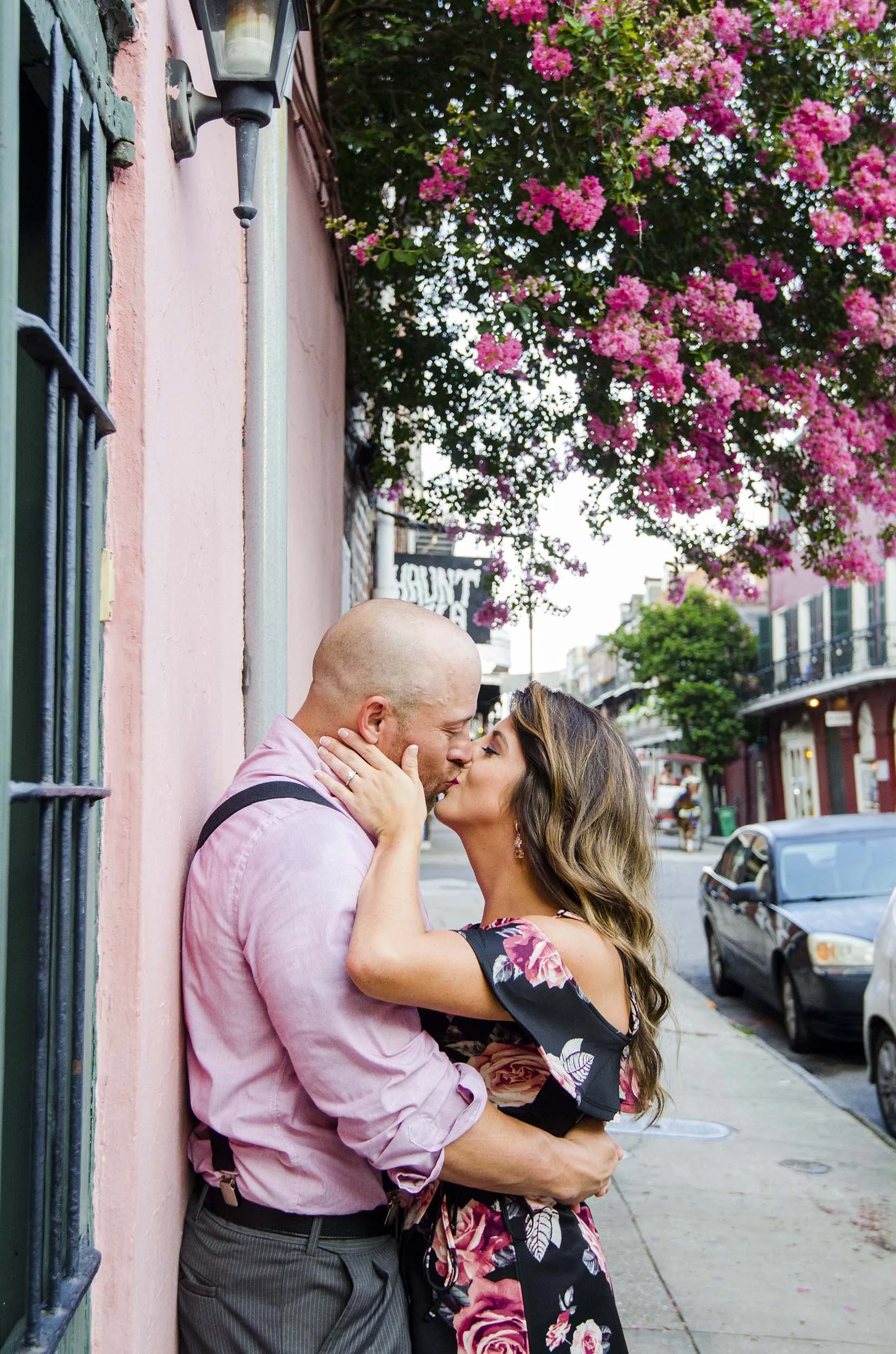 A man and woman embracing in a kiss on a New Orleans French Quarter street with pink flowering tree in the background.