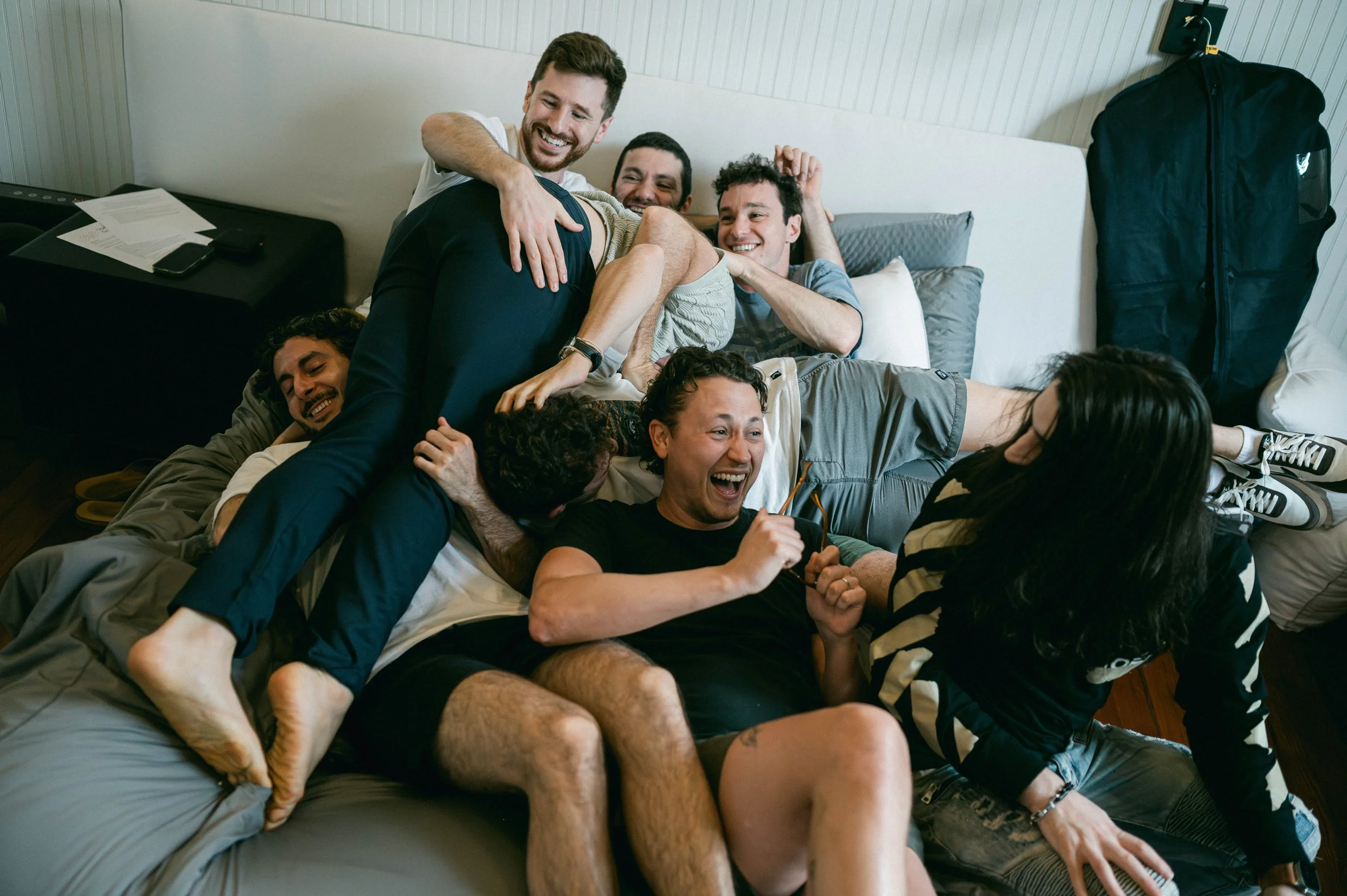 A groom and his groomsmen playing and laughing together on a bed.