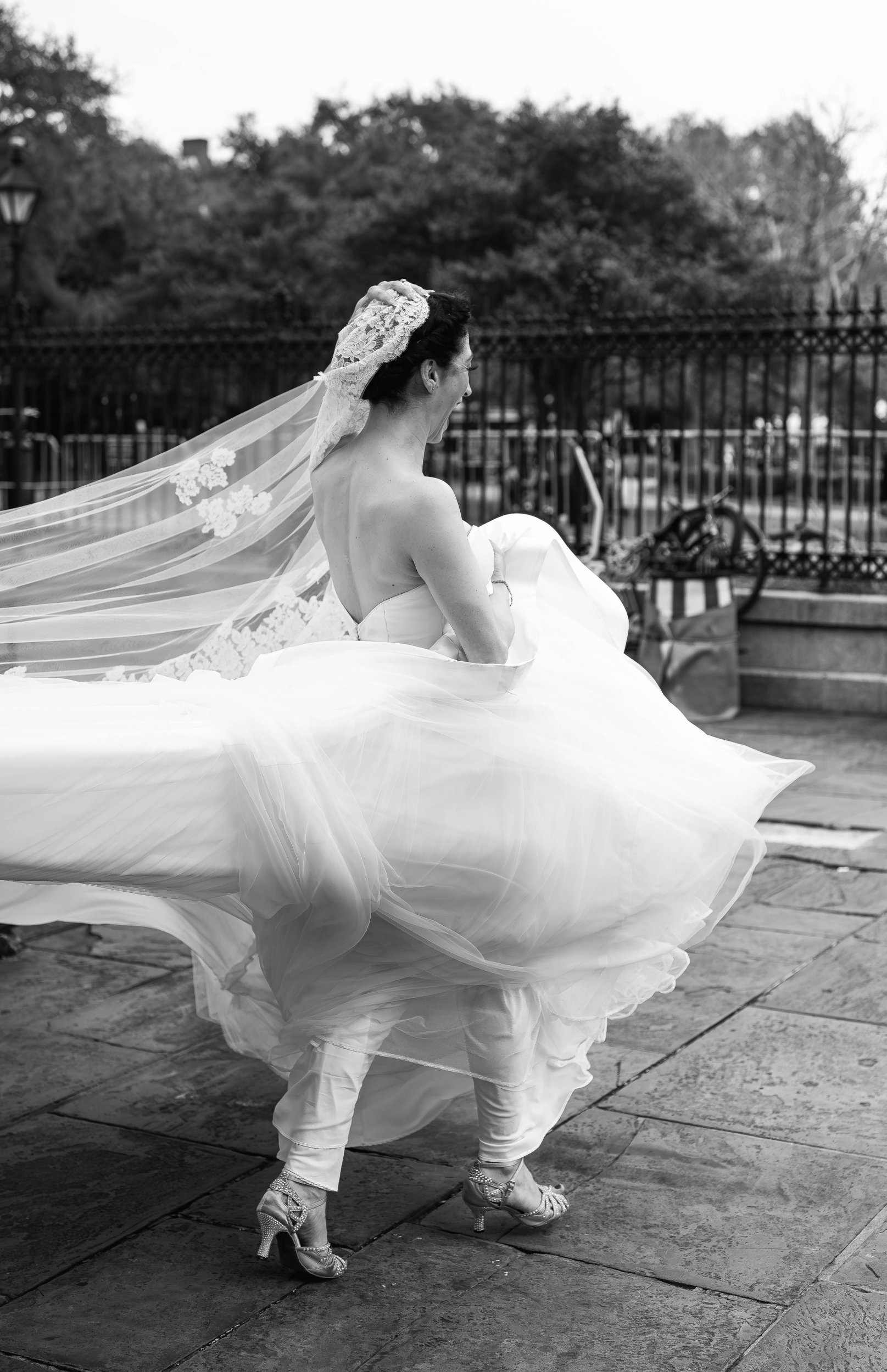 A woman in a wedding dress spinning and twirling outdoors, with her veil flowing behind her, in New Orleans.