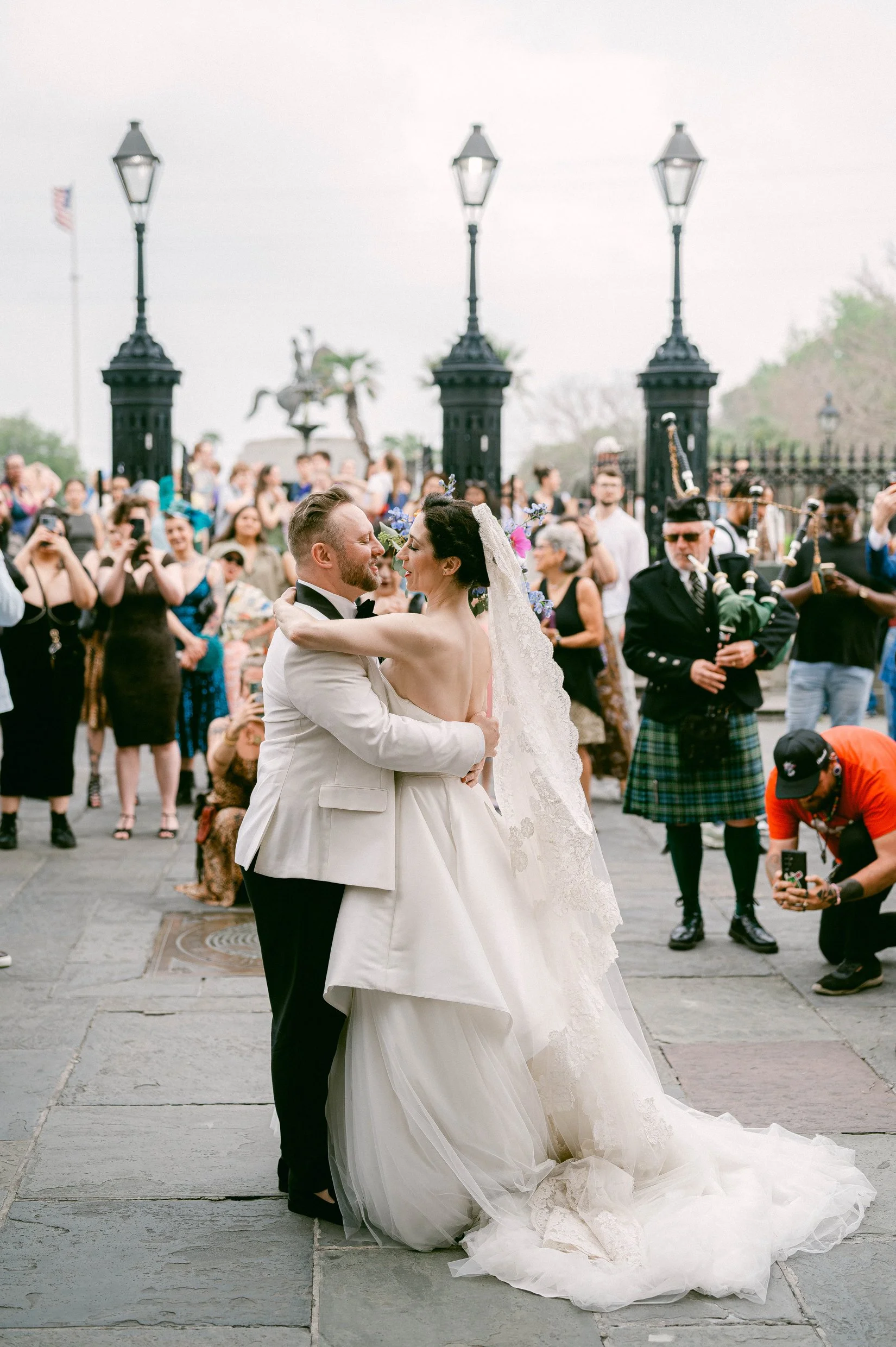 A newly married couple embrace and look at each other while surrounded by guests and a bagpiper in New Orleans French Quarter.