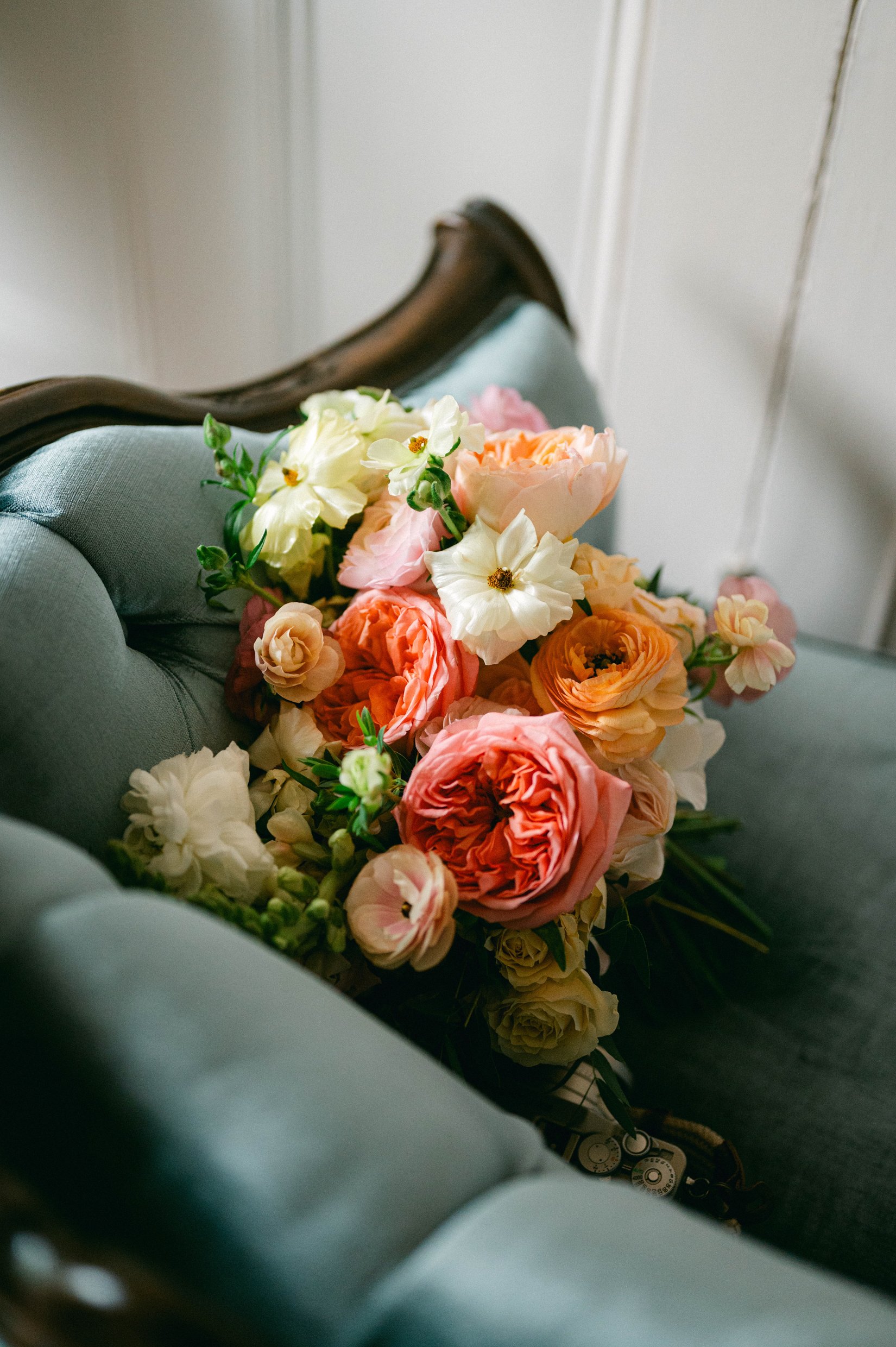 A bouquet of pink and white flowers resting on a light blue upholstered sofa with a wooden frame.