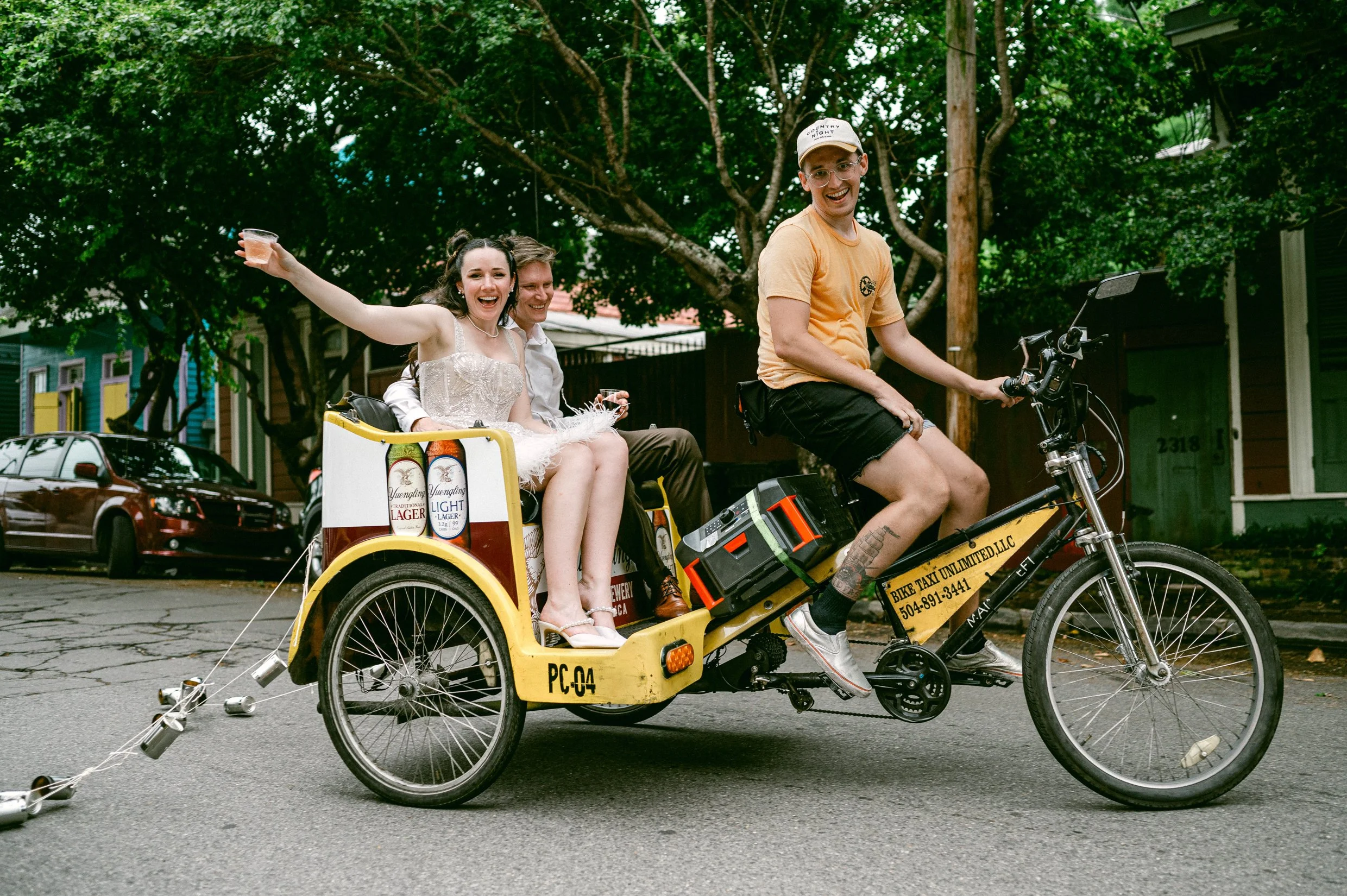 A bride and groom riding in a bicycle taxi adorned with a "Just Married" sign and tin cans after their wedding.