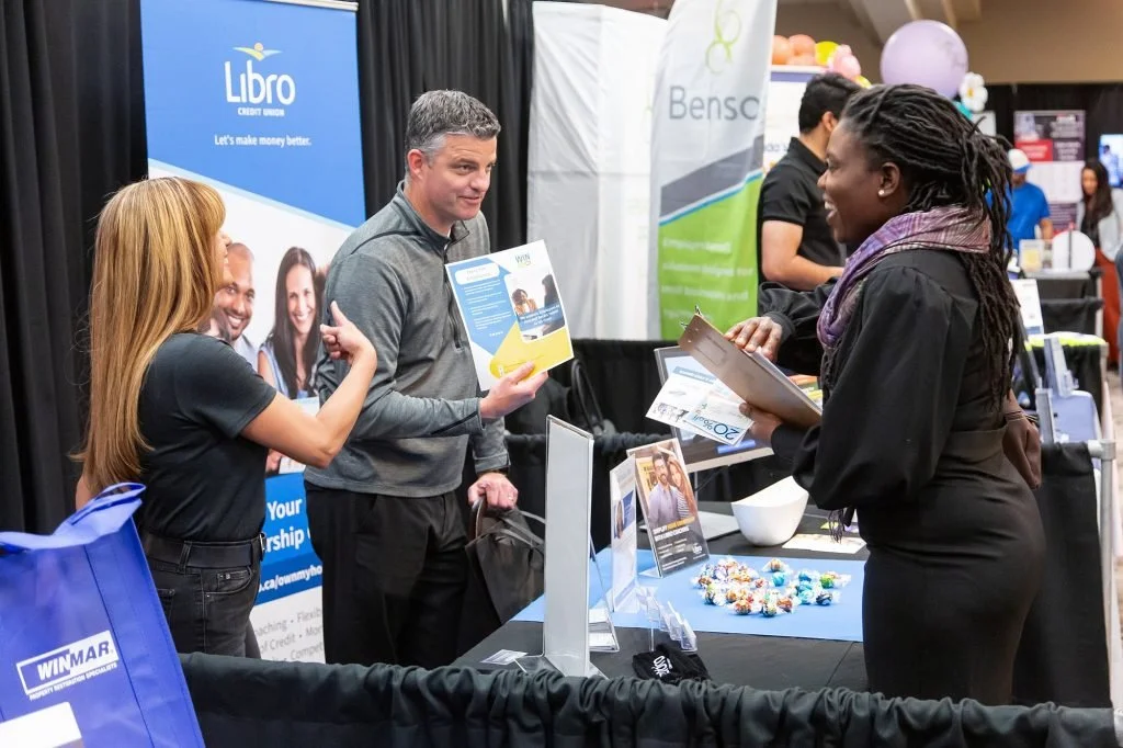 People talking at a booth with banners and promotional materials at a trade show or conference.