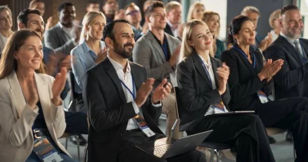 People sitting in an audience at a conference, clapping and smiling.