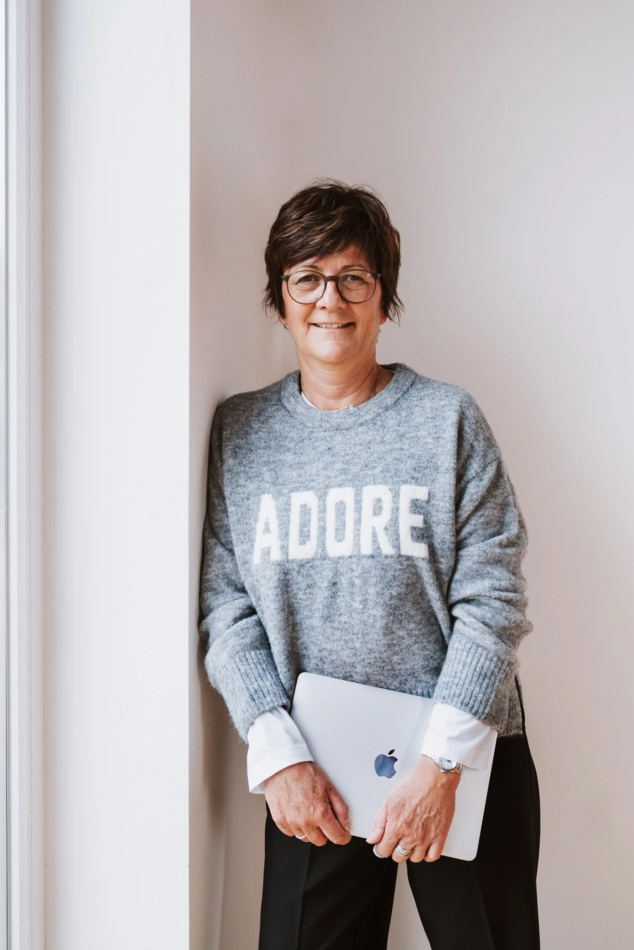 Onika hält einen MacBook-Laptop und lehnt an die Wand.