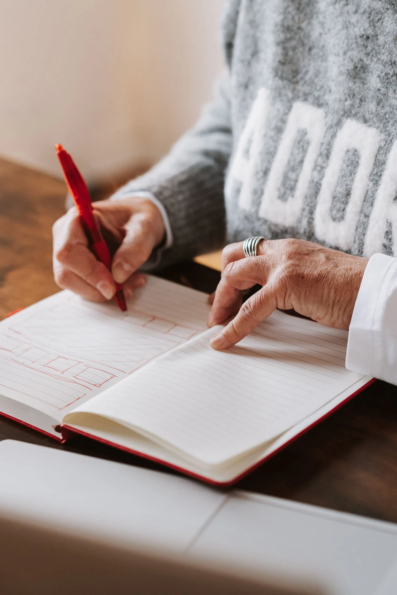 Onika schreibt in ein geöffnetes Notizbuch mit rotem Stift, sitzt an einem Holztisch.