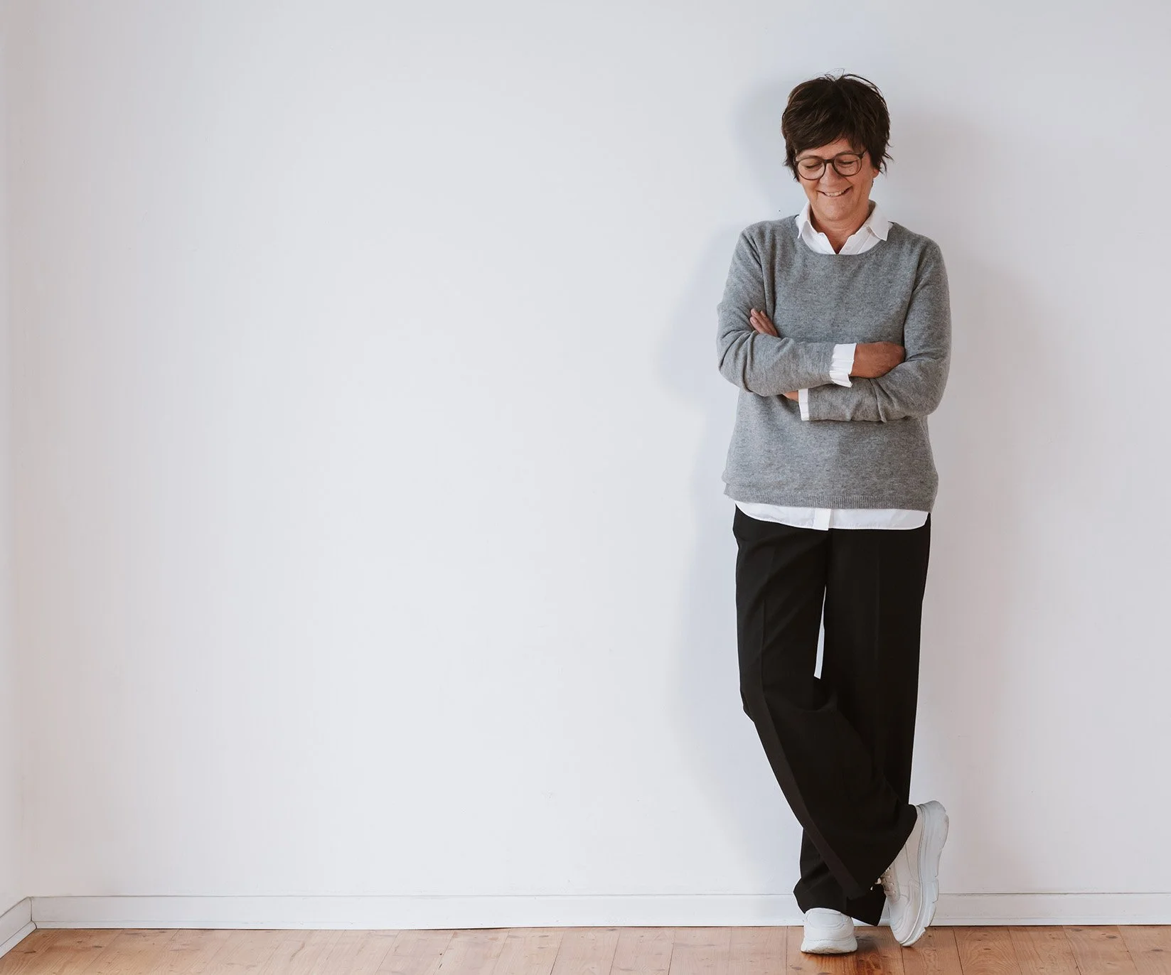 Onika in lässiger Kleidung lehnt an weißer Wand, lächelt