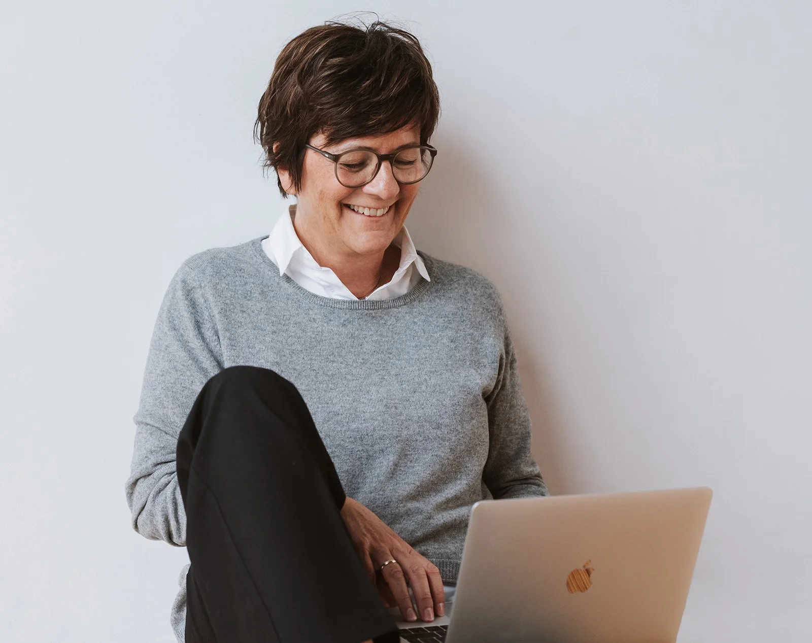Onika sitzt vor einem Laptop, trägt einen grauen Pullover und eine weiße Bluse.