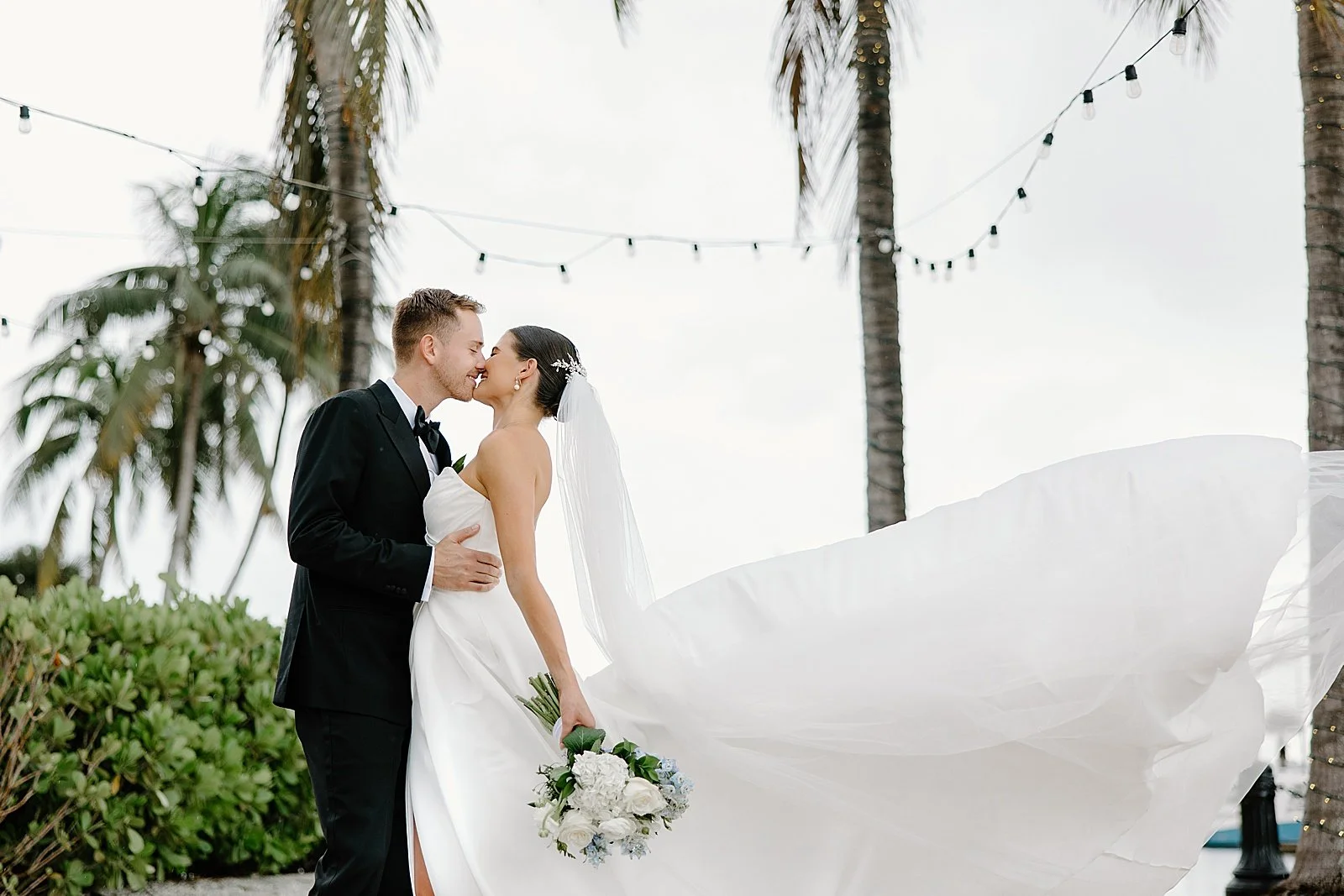 man kisses wife under tropical trees by ocean by Taylor Shea Photo