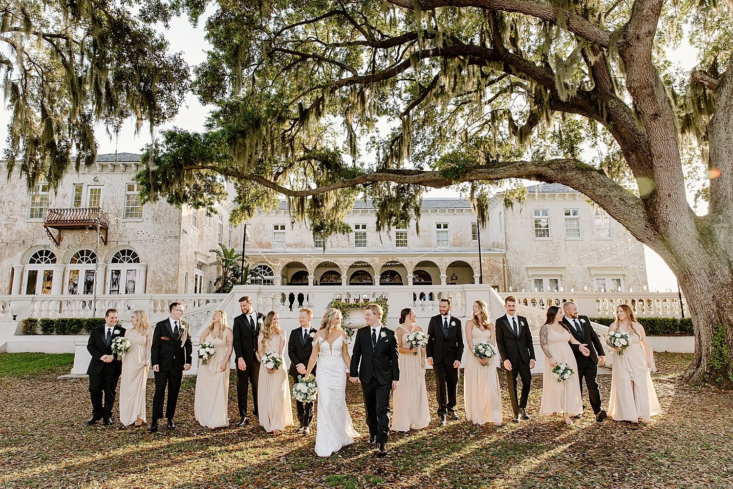  bridesmaids in blush pink walk with groomsmen and happy couple on lawn by Florida wedding photographer 