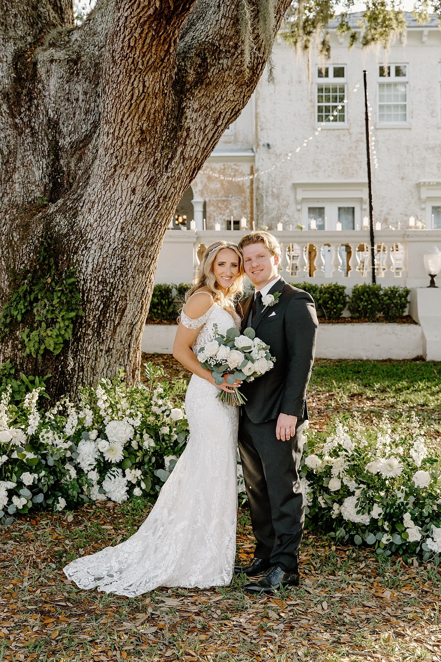  husband and wife under large tree during golden hour after ceremony at Bella Cosa 