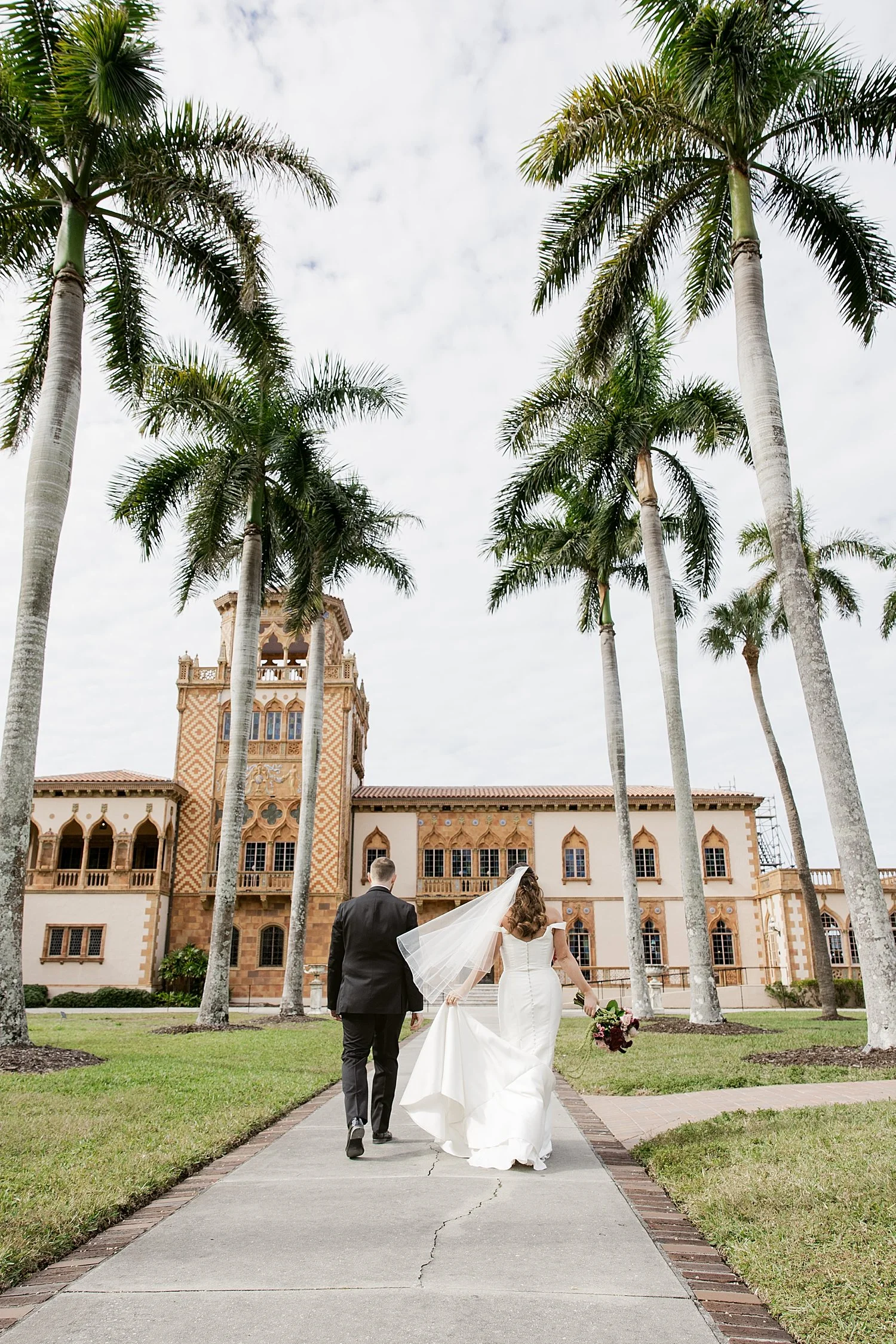  husband and wife walk down pathway lined by palm trees by Taylor Shea Photo 