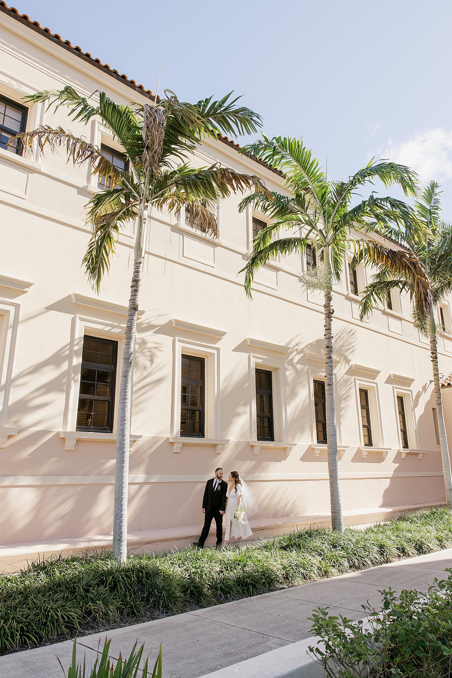  husband and wife stroll the sidewalk under palm trees after their courthouse elopement 