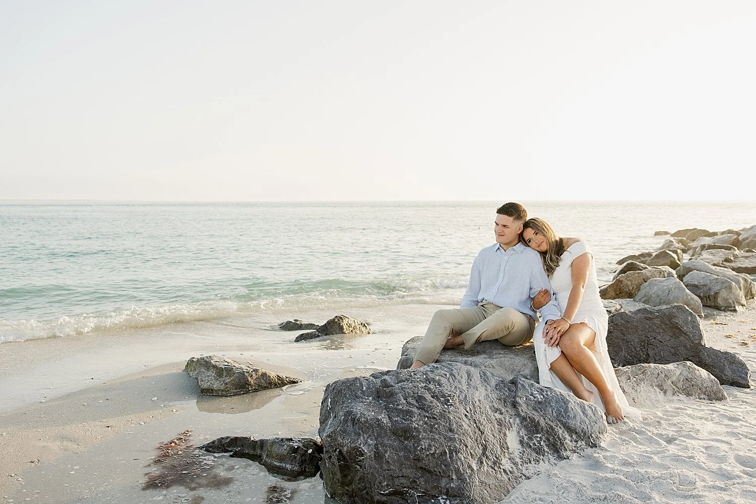 man and woman sit on large rock next to ocean on Boca Grande Island 