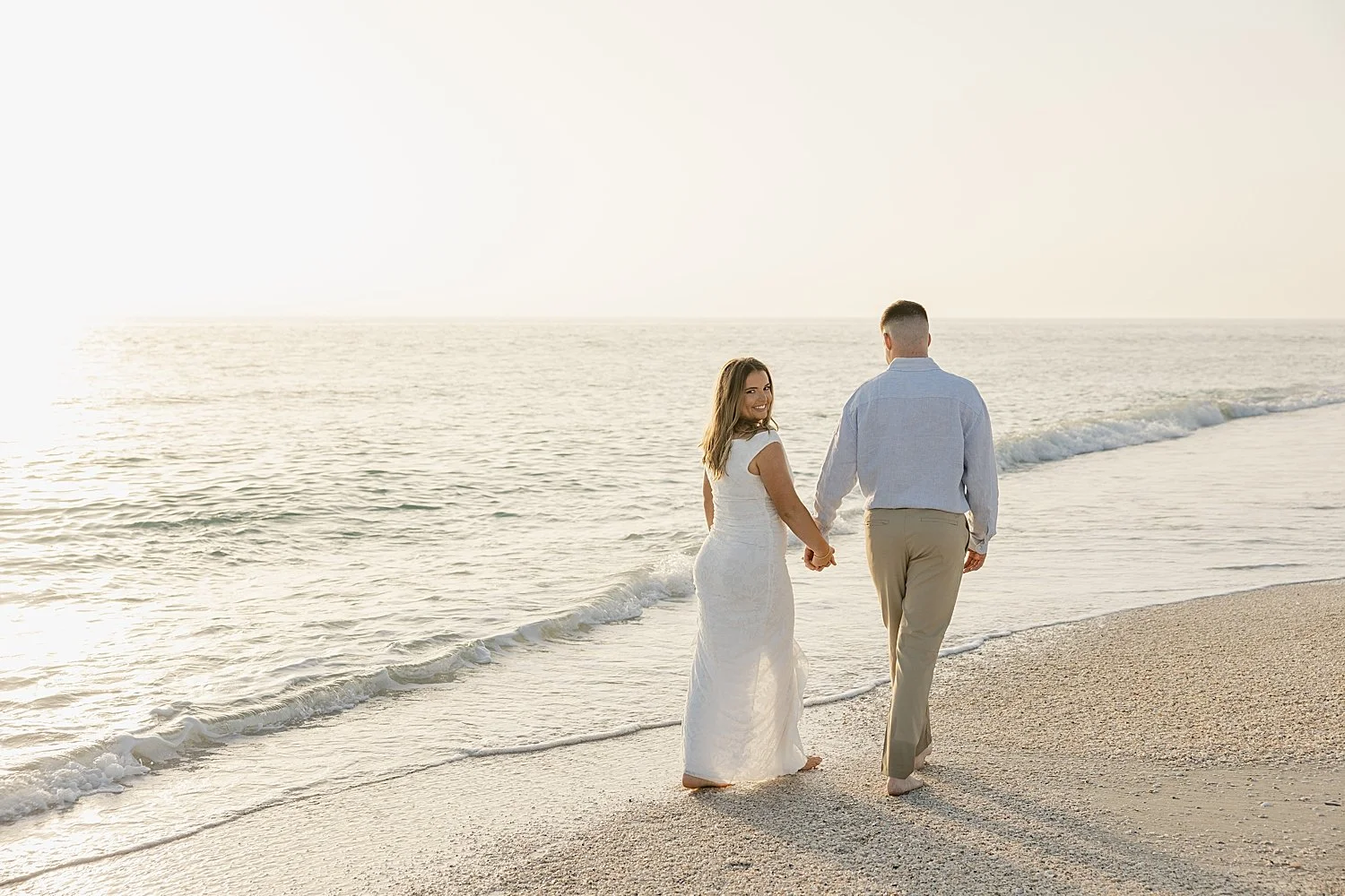  couple walks hand in hand down the shoreline at sunset by Florida wedding photographer 