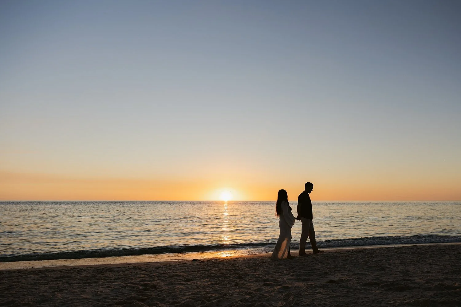  couple walks hand in hand down beach at sunset by Taylor Shea Photo 