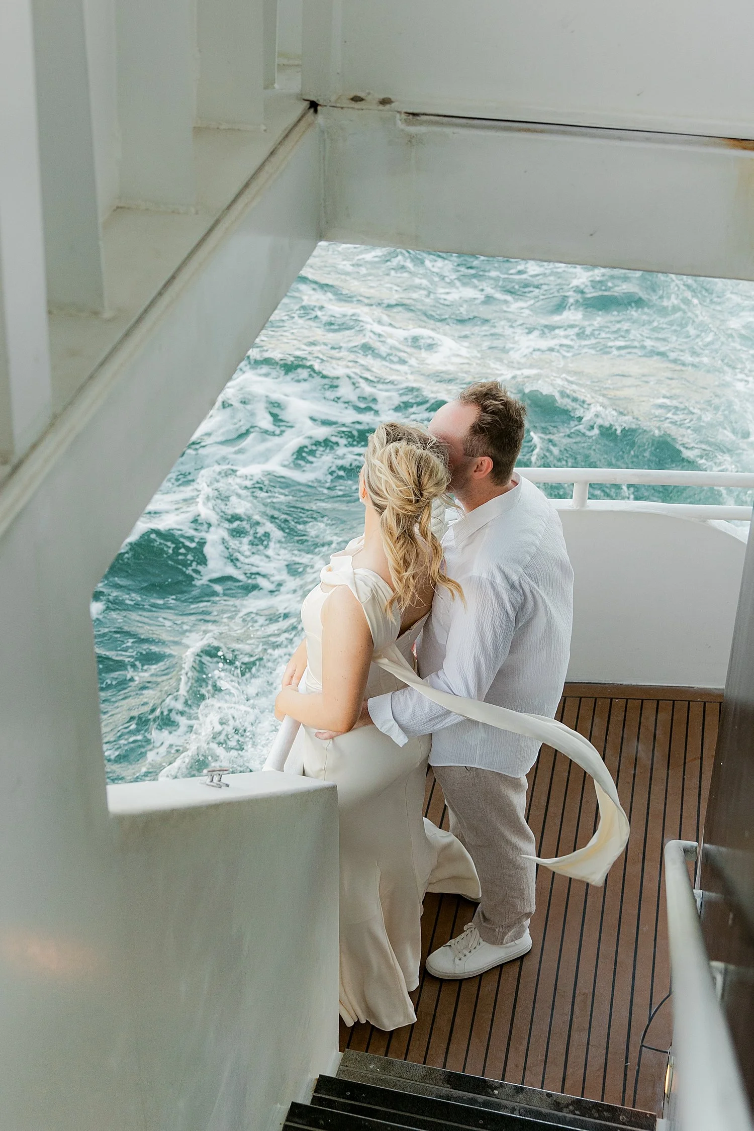  bride and groom stand against railing looking at water for wedding weekend on yacht 