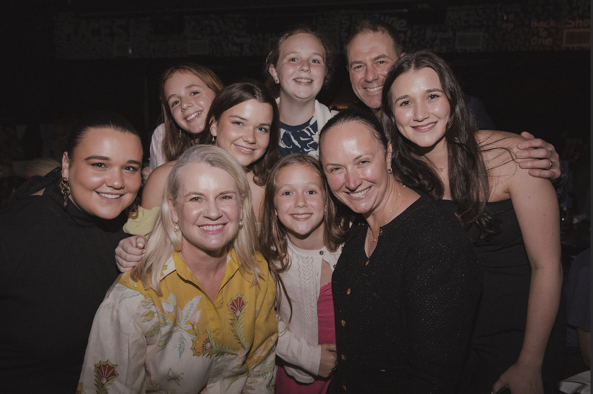A group of ten people, including adults and children, smiling and cheering together at a social gathering.
