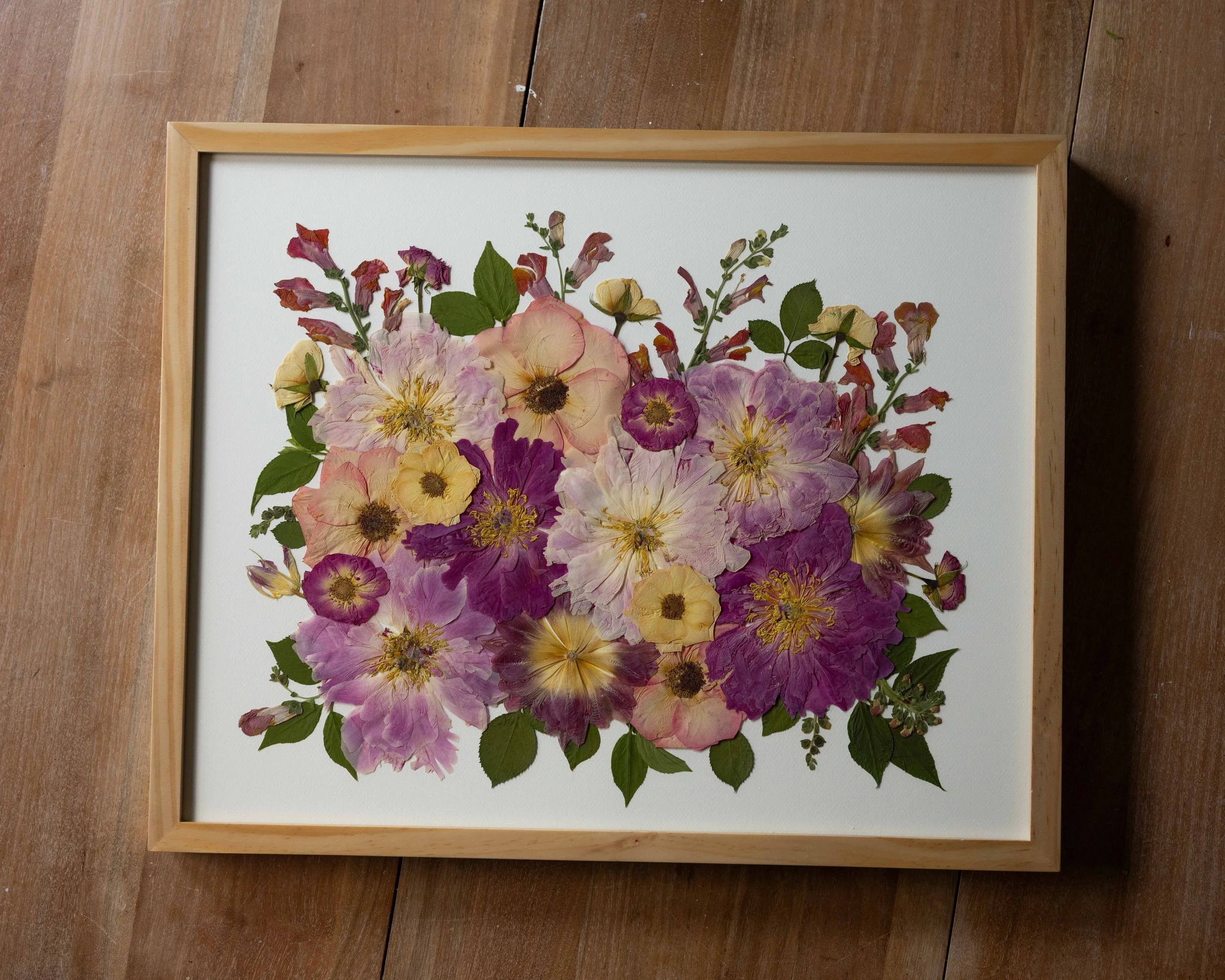 framed pressed flower wedding bouquet with different flowers like roses, peonies, and snapdragons in shades of pink, peach, and orange.