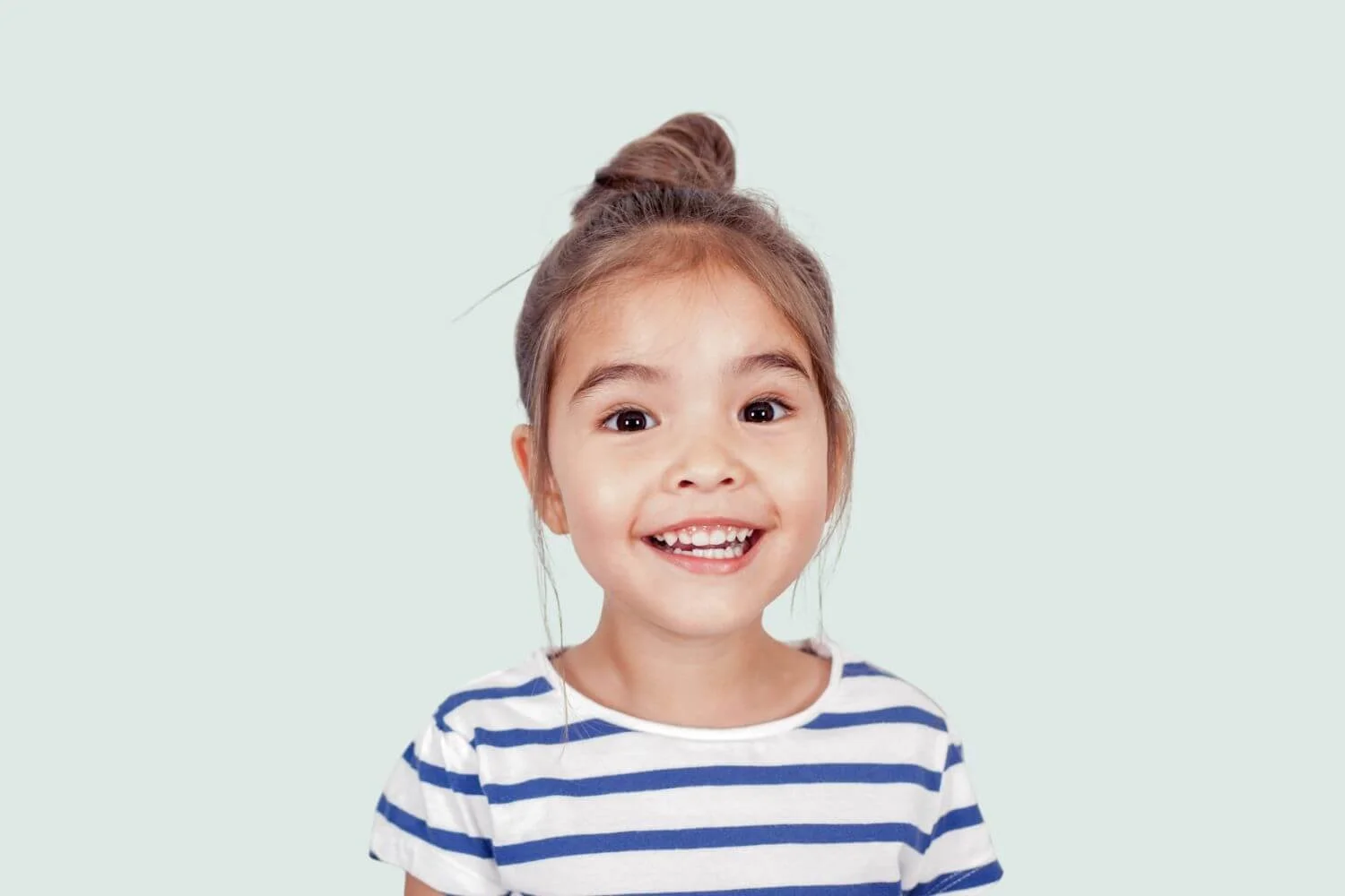 Young girl smiling with bun in her hair wearing a blue and white striped shirt.