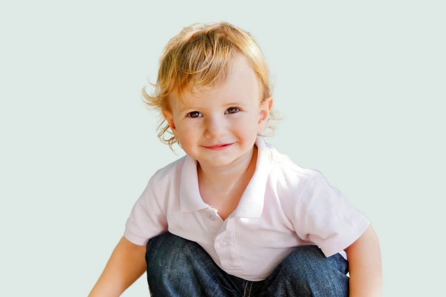 Toddler with light hair sitting and smiling.