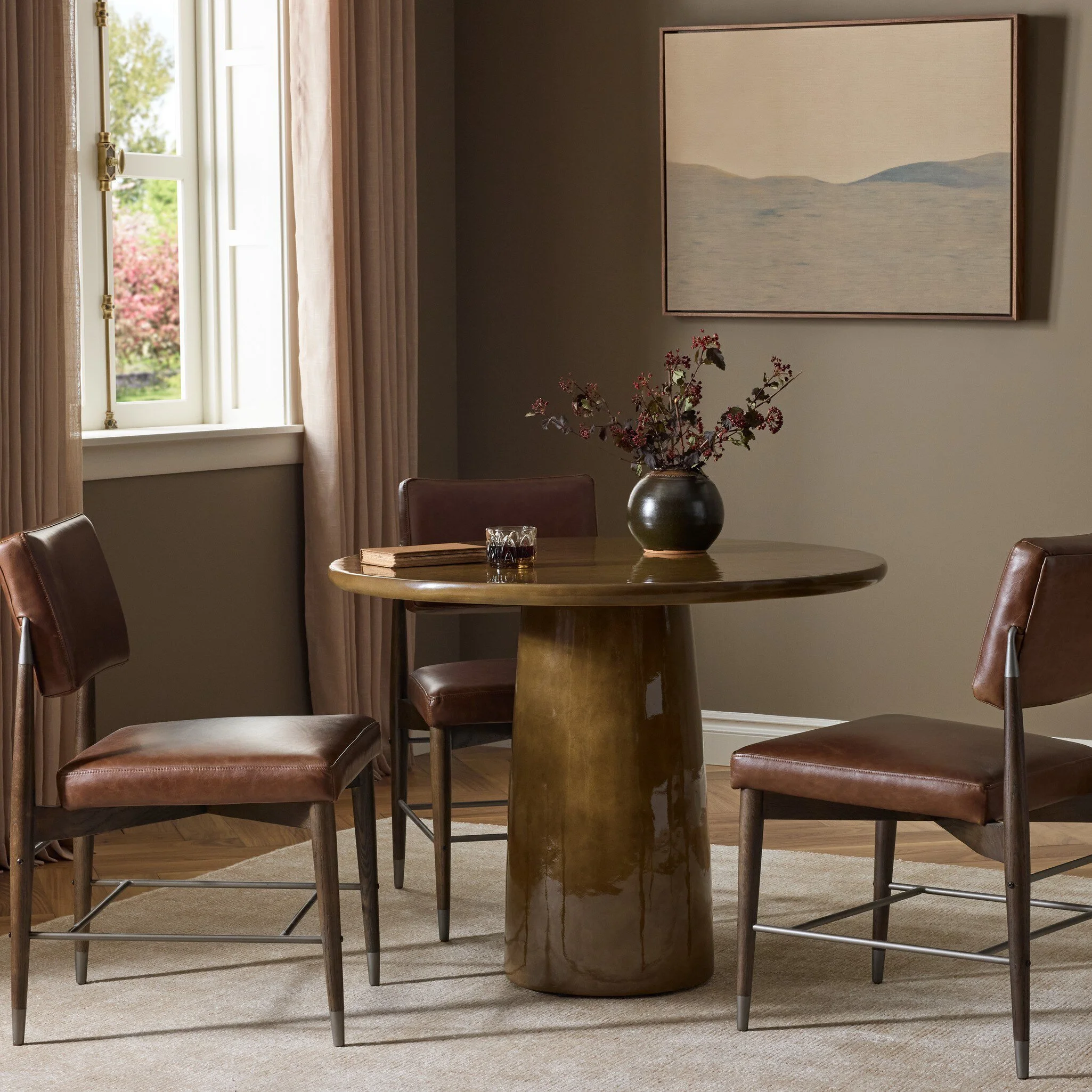 Dark wood console table with fresh flowers and a black lamp. There is a landscape painting above in neutral colors.