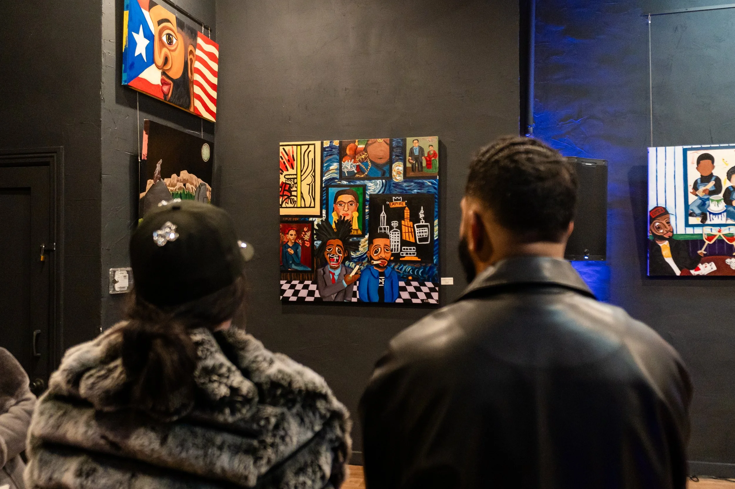Two people viewing colorful paintings in an art gallery with black walls and dim lighting.