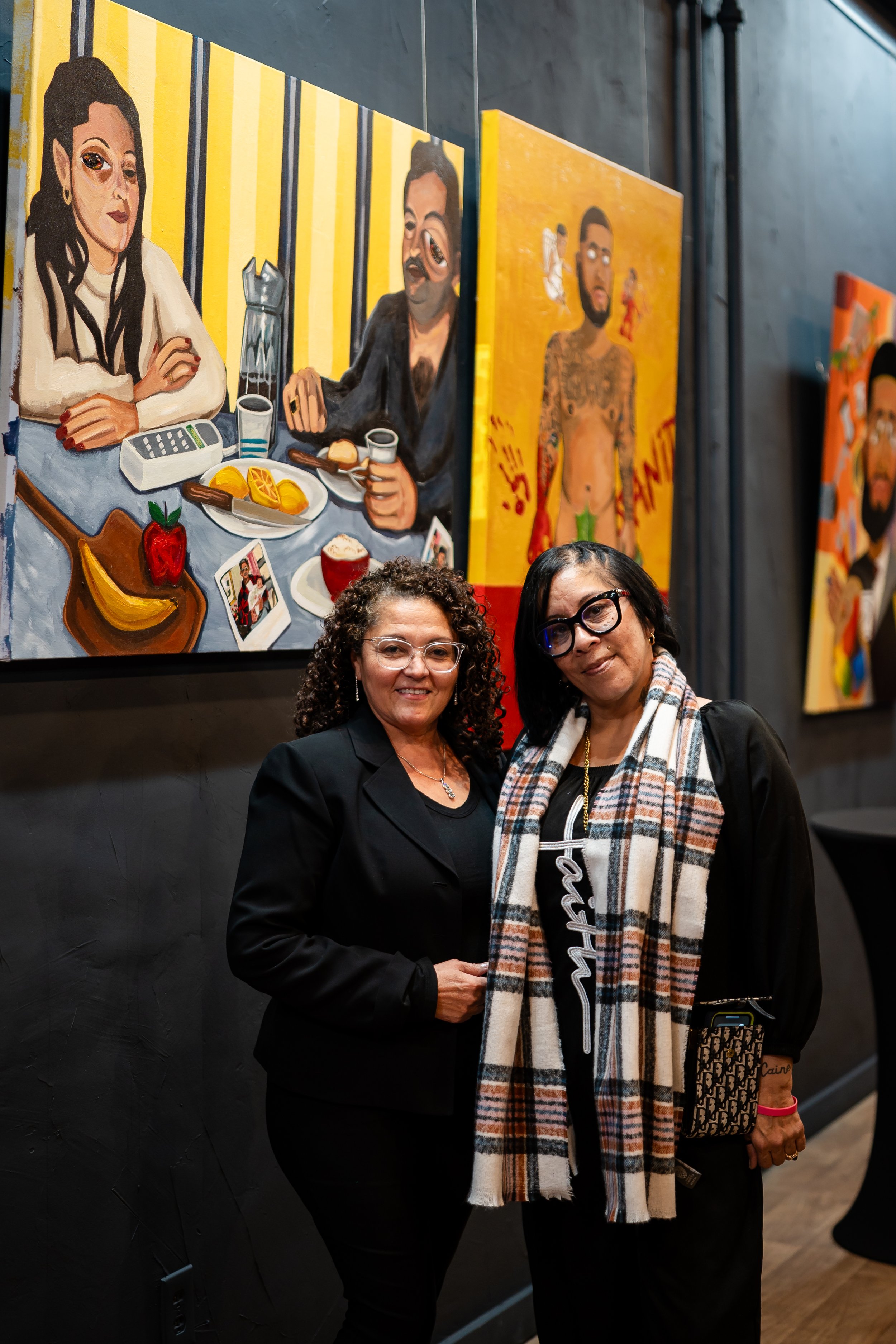 Two women standing in front of colorful paintings in an art gallery.