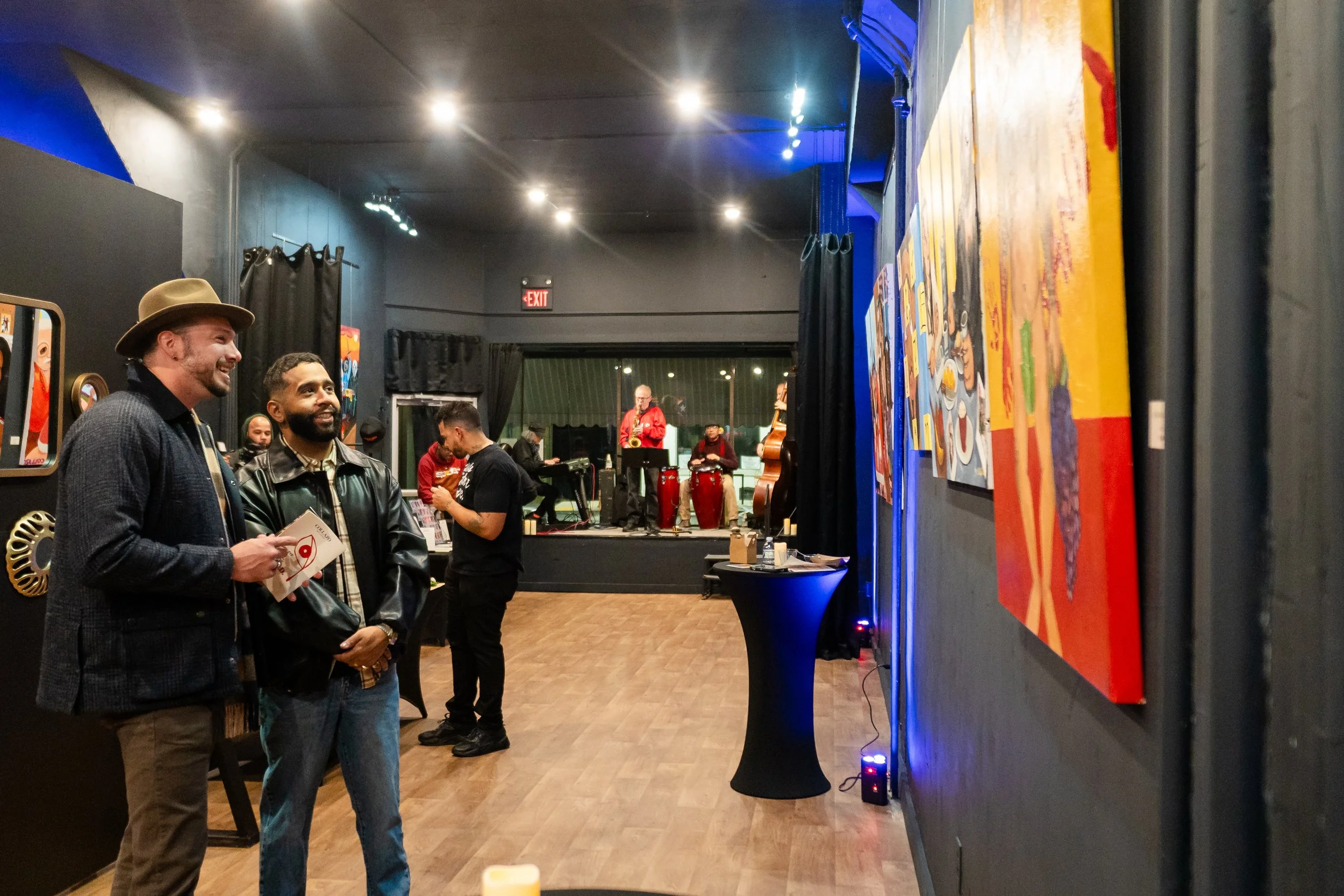 People viewing artwork in an art gallery with a live music performance in the background.